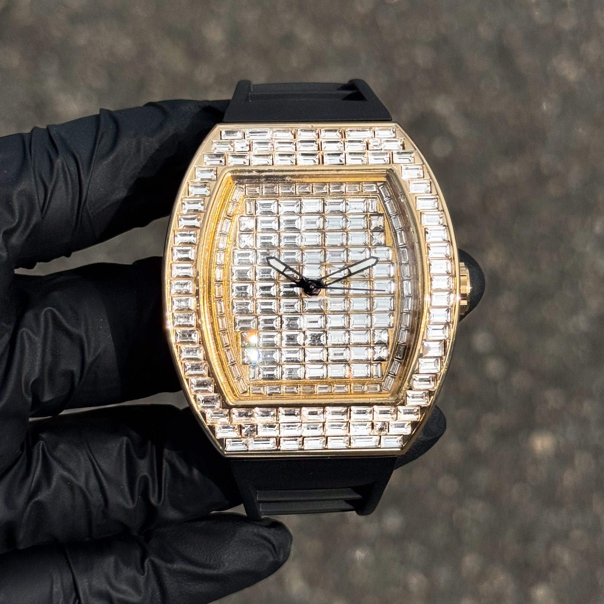 Gold 43mm iced out tonneau watch with full baguette crystal dial and black silicone band for men.