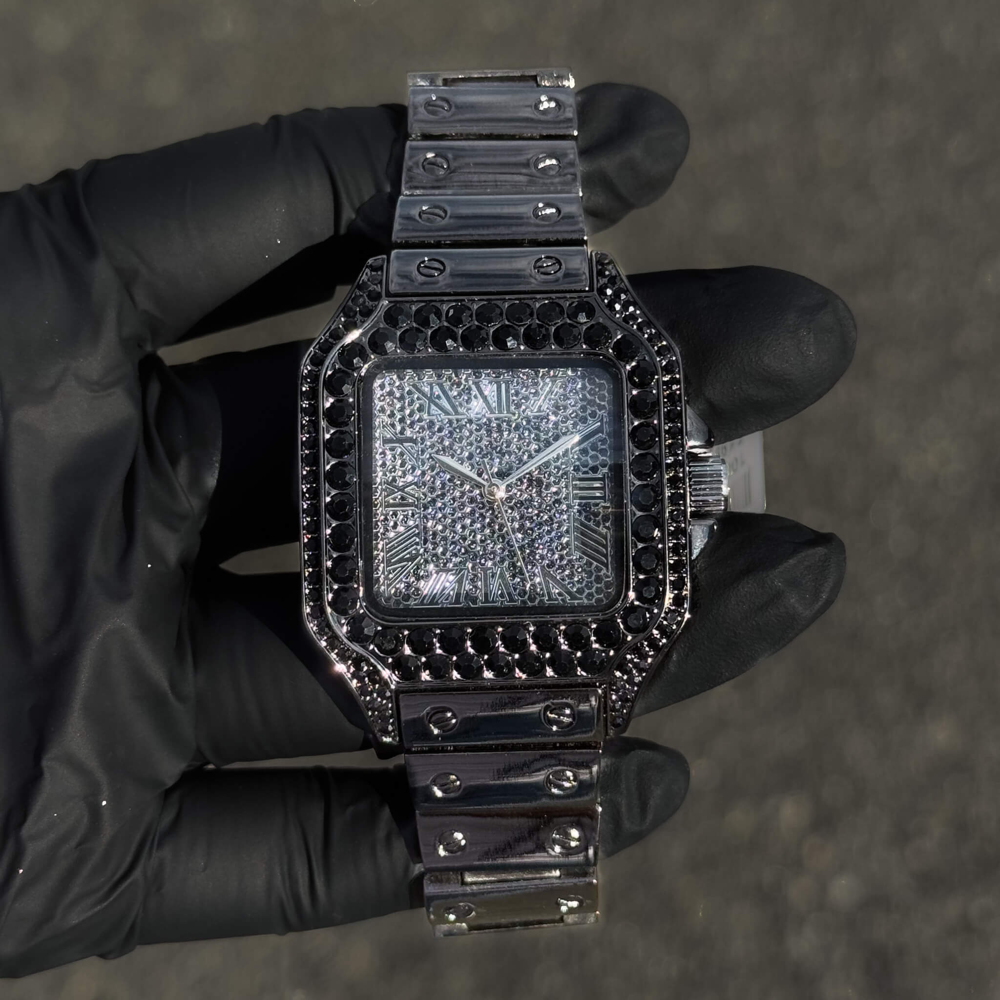 Black 40mm iced out square men’s watch with dark stones, crystal dial and steel bracelet.