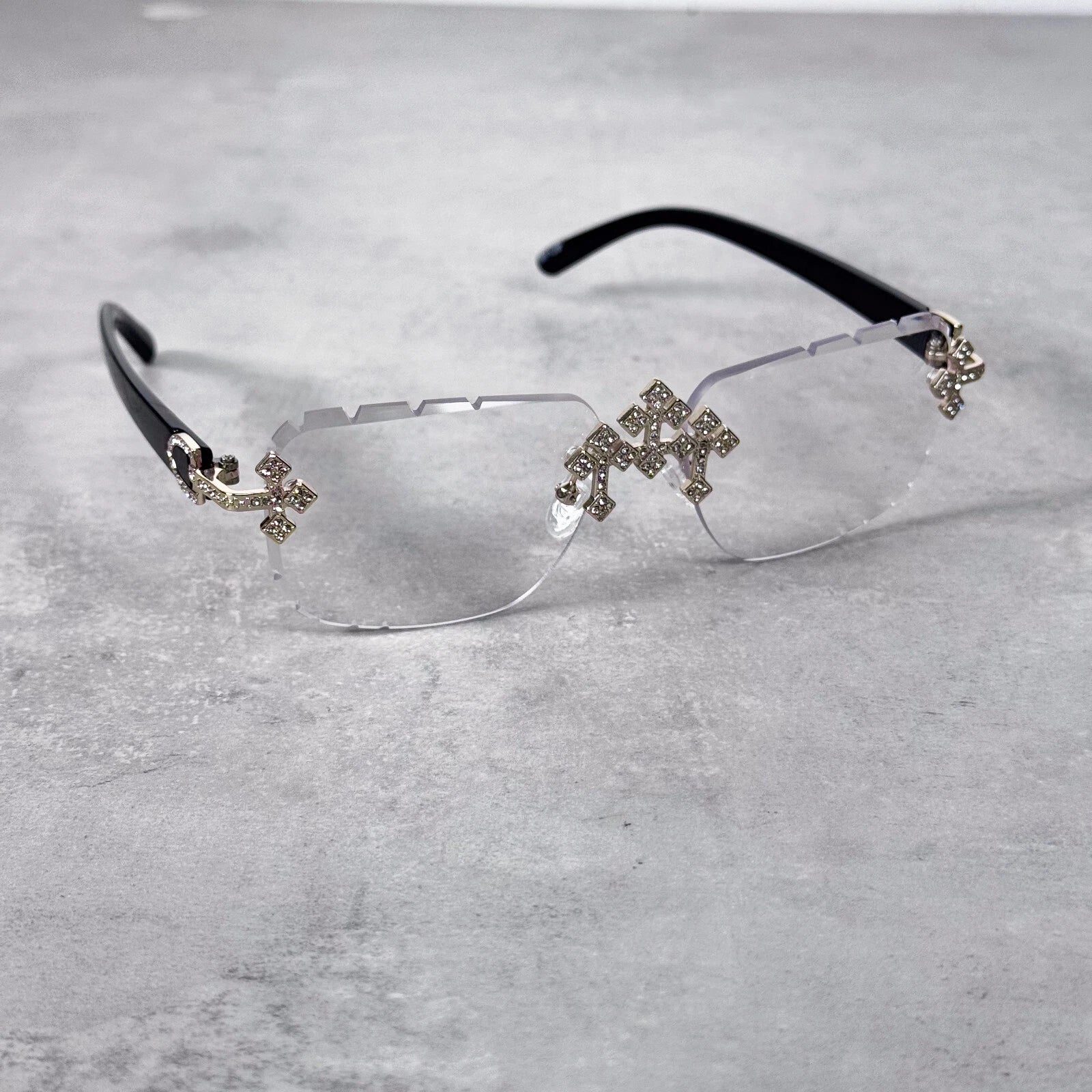 Rimless clear lens sunglasses with crystal cross embellishments and sleek black temples.