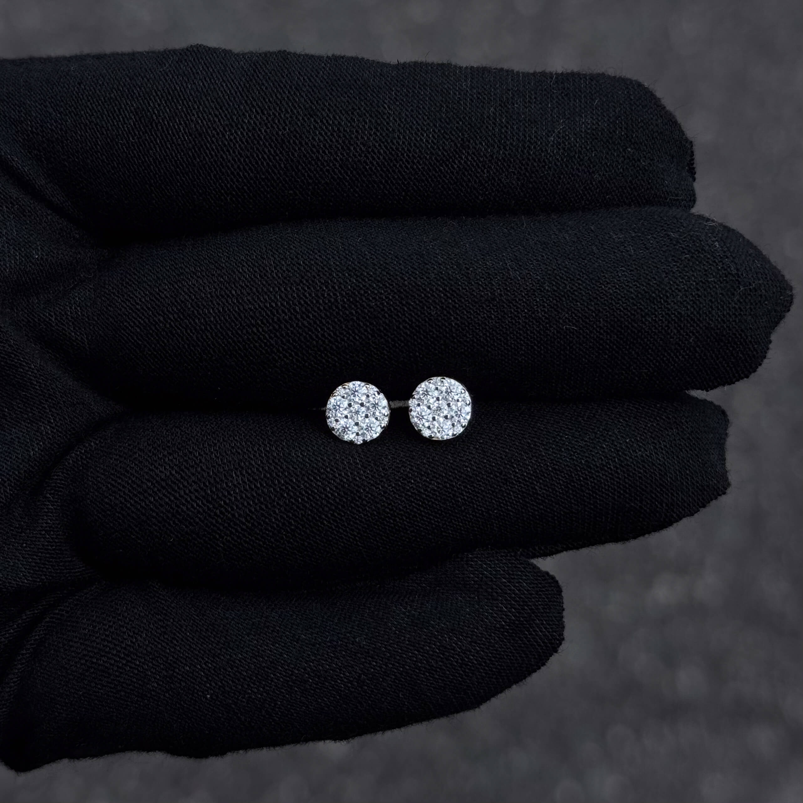 Small round sterling silver moissanite cluster stud earrings with 0.58ct diamonds shown on black glove.
