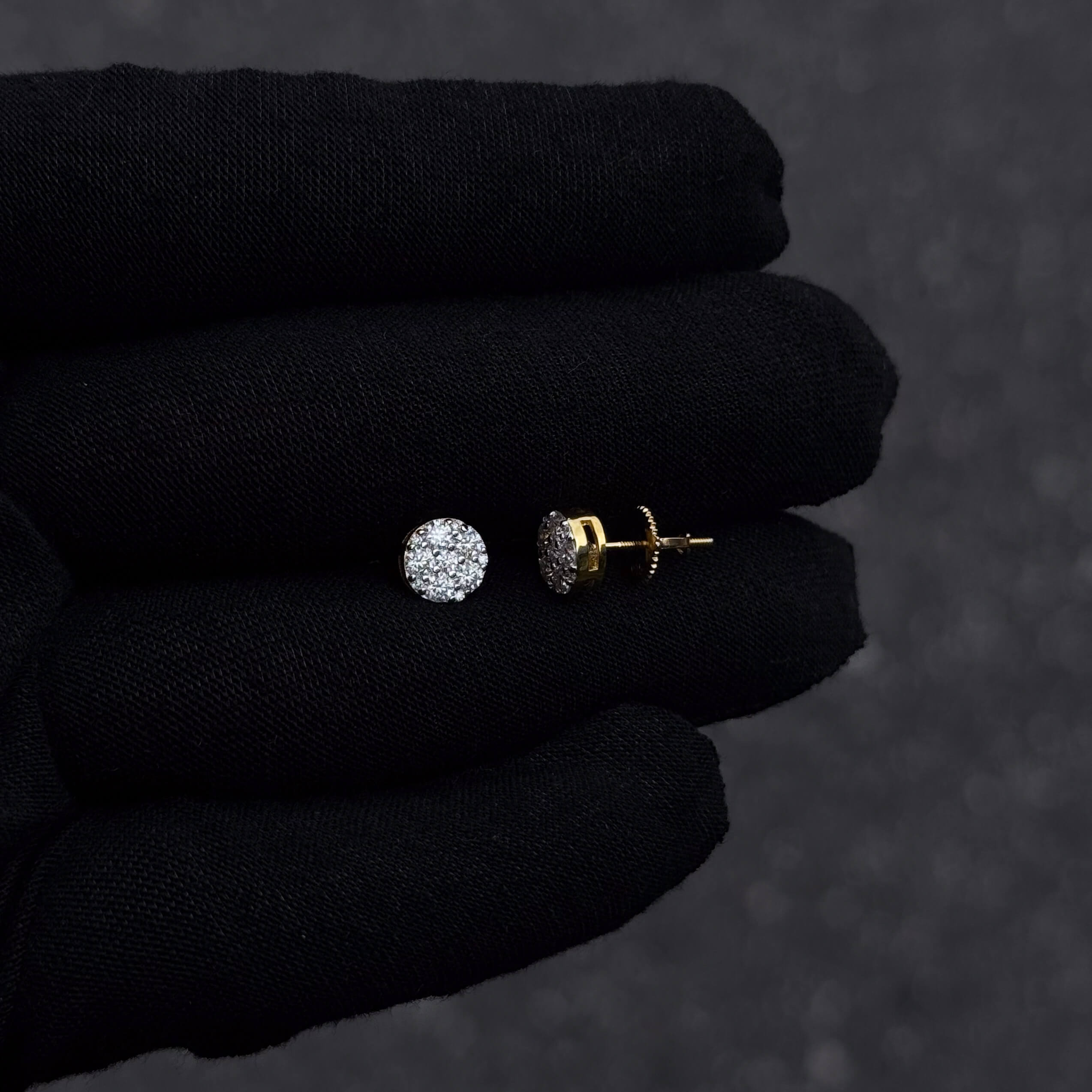 Gold-plated 7mm round moissanite cluster diamond stud earrings with screw backs shown on black glove.