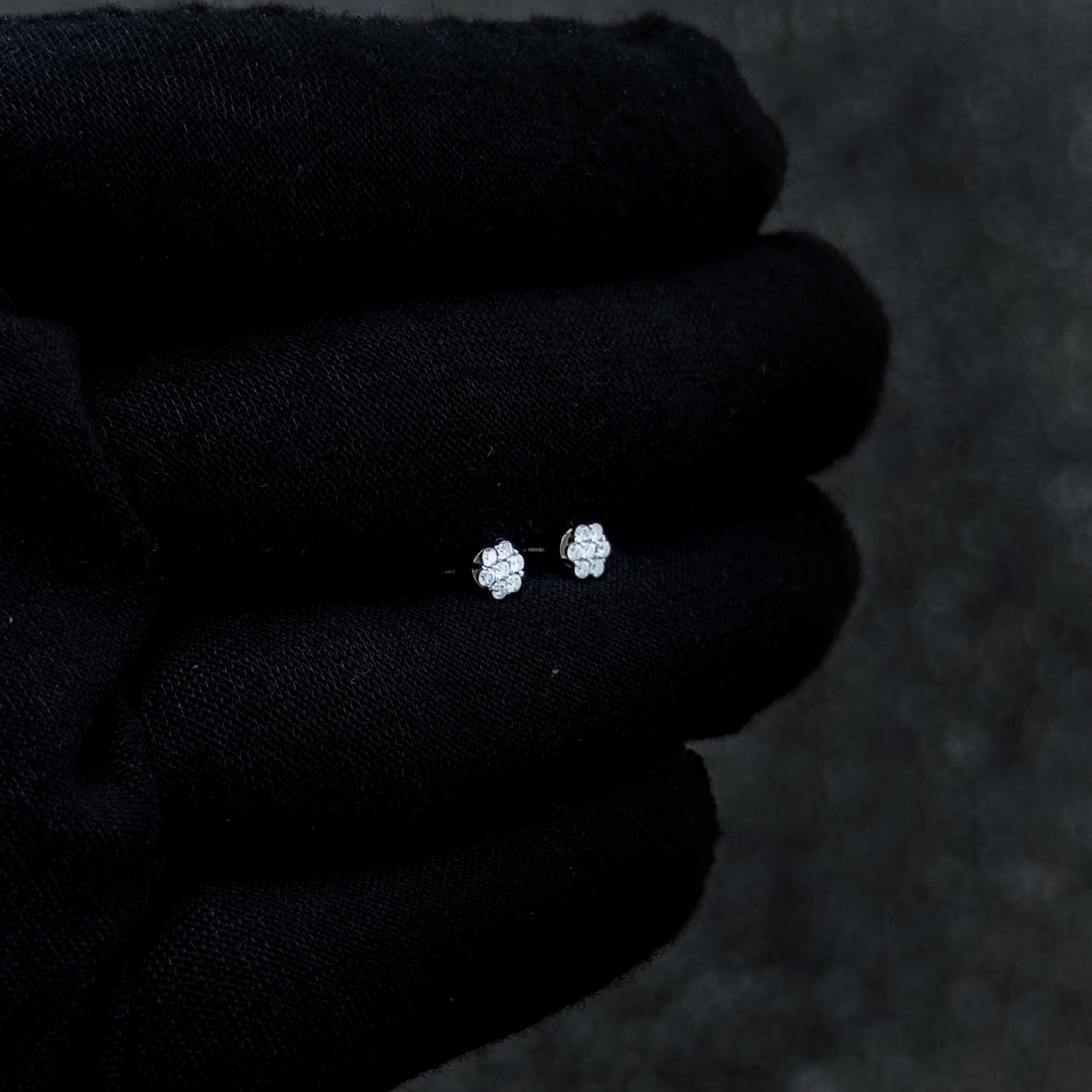 Small sterling silver moissanite cluster stud earrings shown on black glove background.