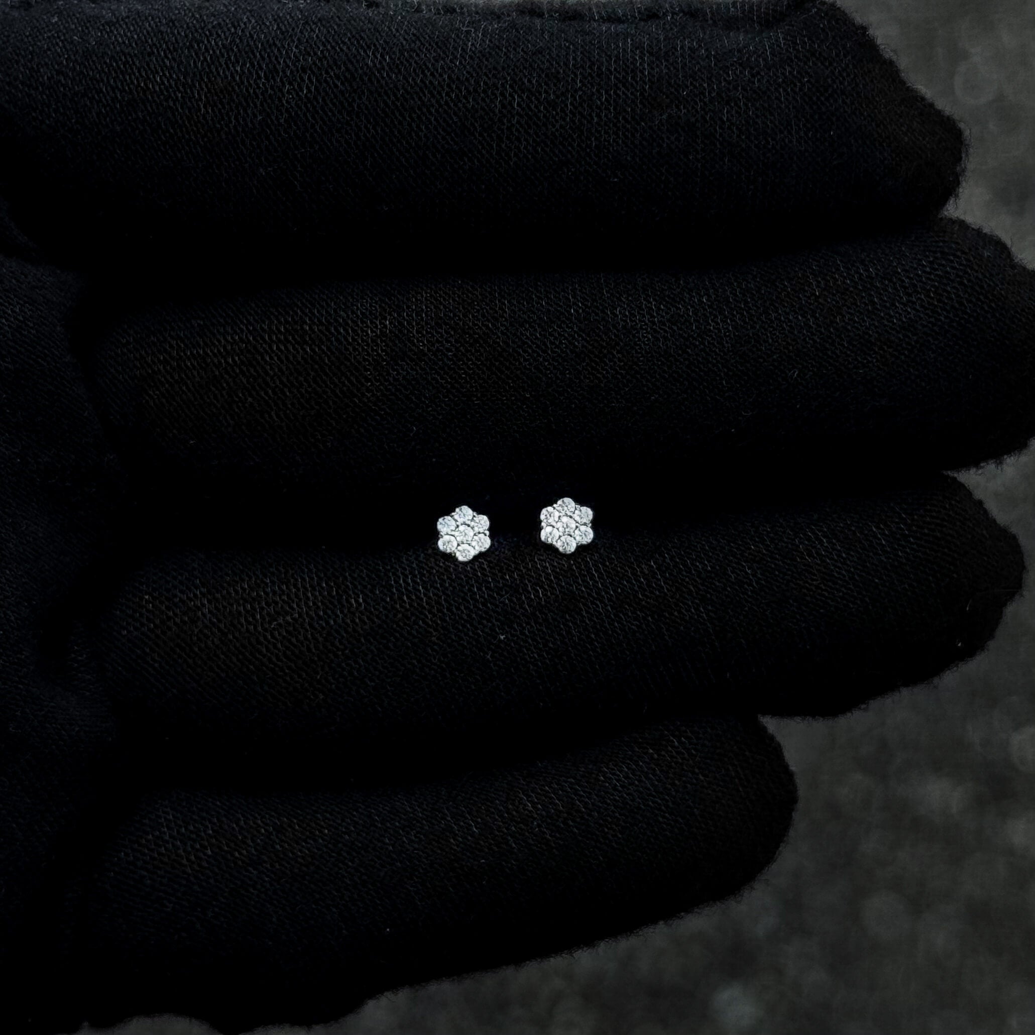 Tiny 5mm flower moissanite diamond studs displayed on black fabric for size reference.