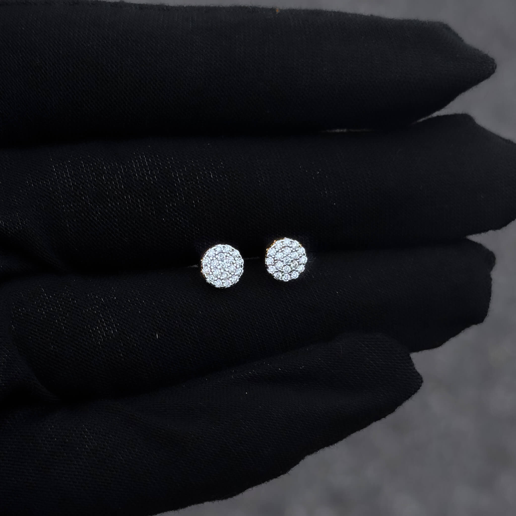 Round moissanite cluster earrings displayed on black glove, pavé diamond studs in silver setting.