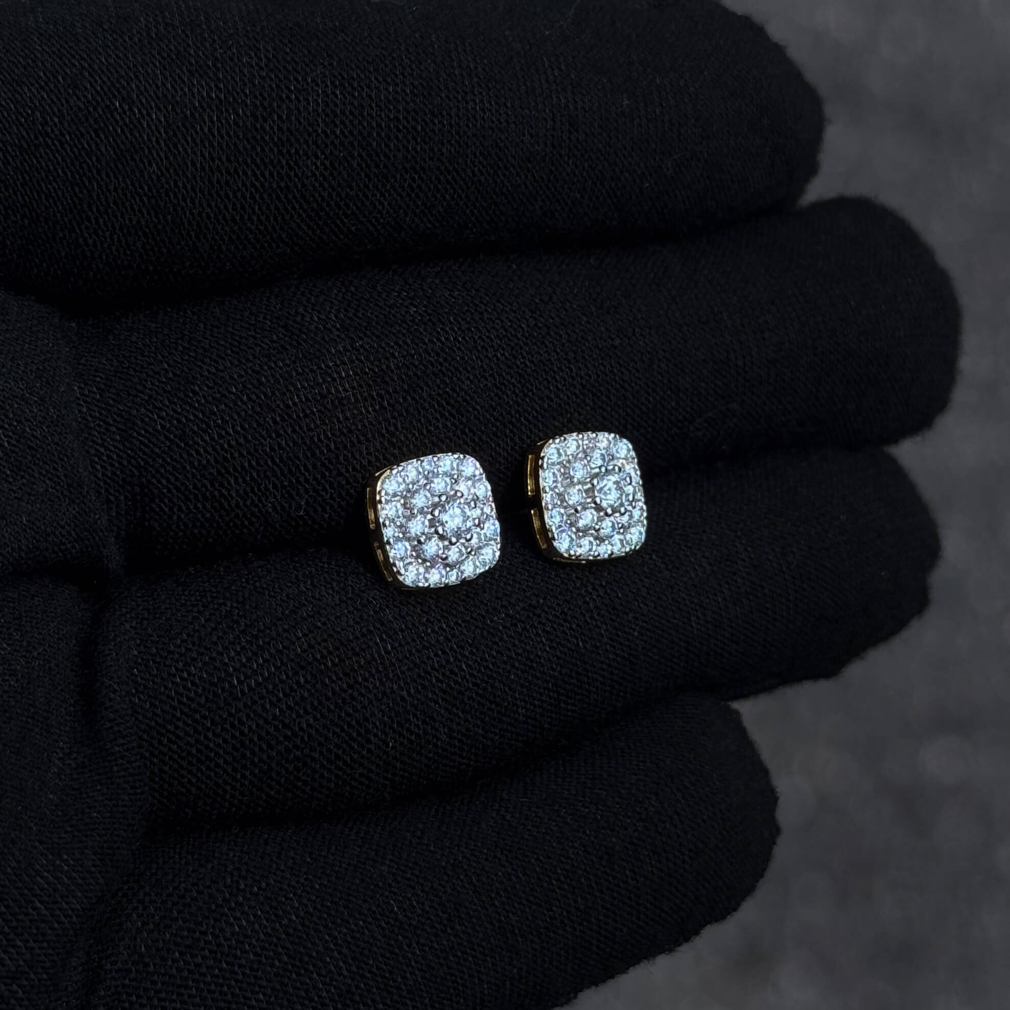 Angled view of square 9mm moissanite cluster earrings with gold backing on black glove.