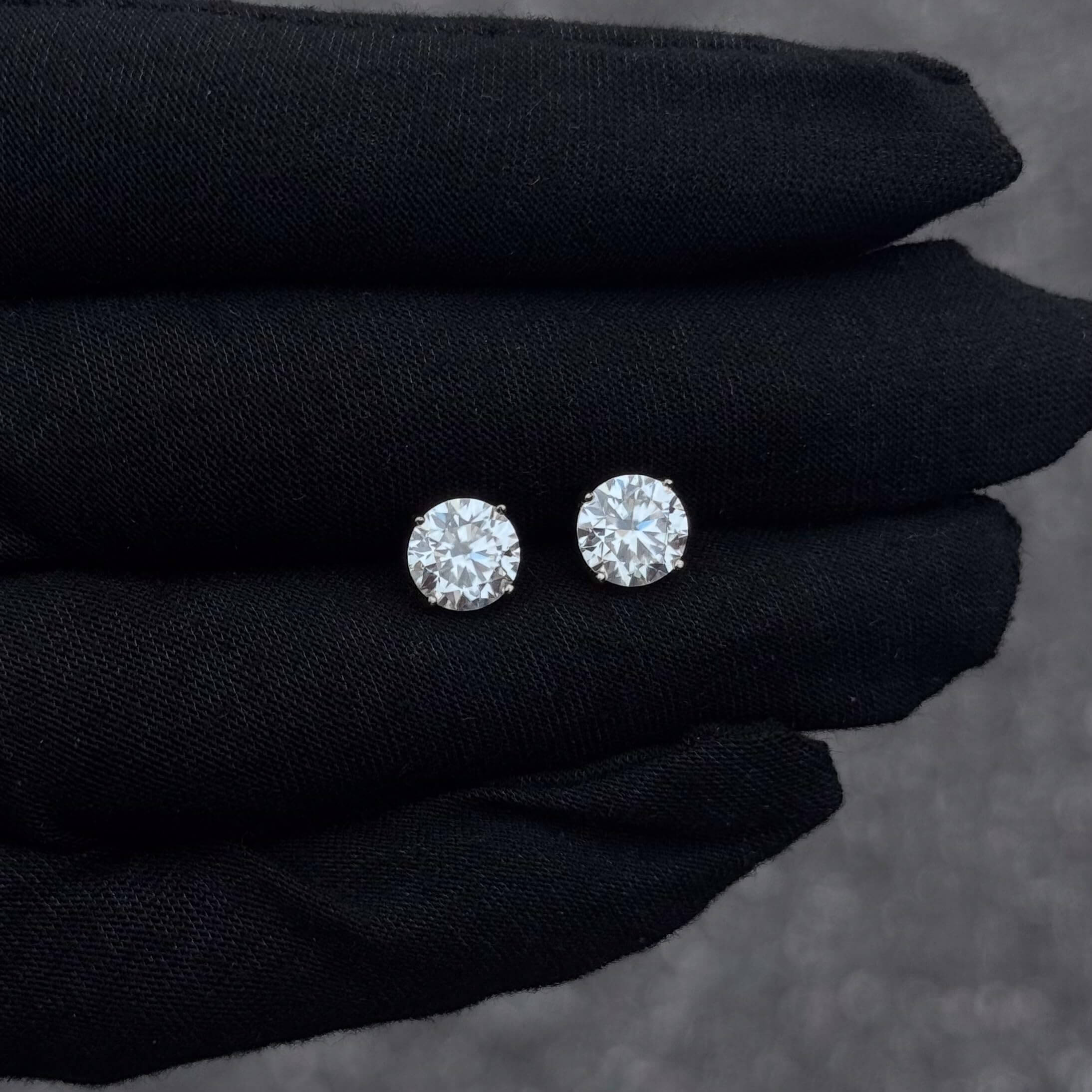 Round 7mm moissanite solitaire diamond studs in sterling silver shown on black glove.