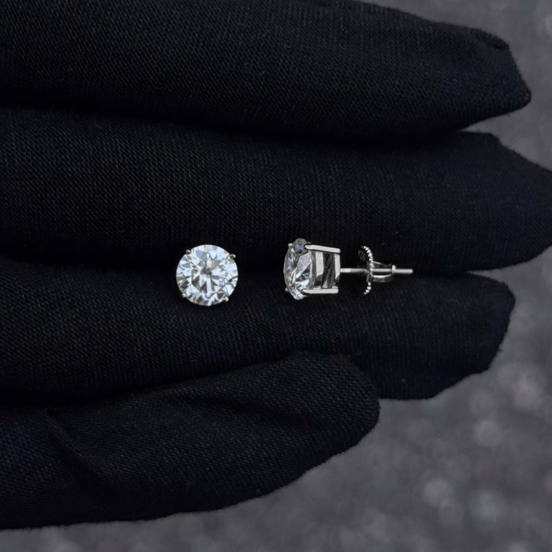 Sterling silver 7mm moissanite solitaire earrings with screw-back posts on black glove.