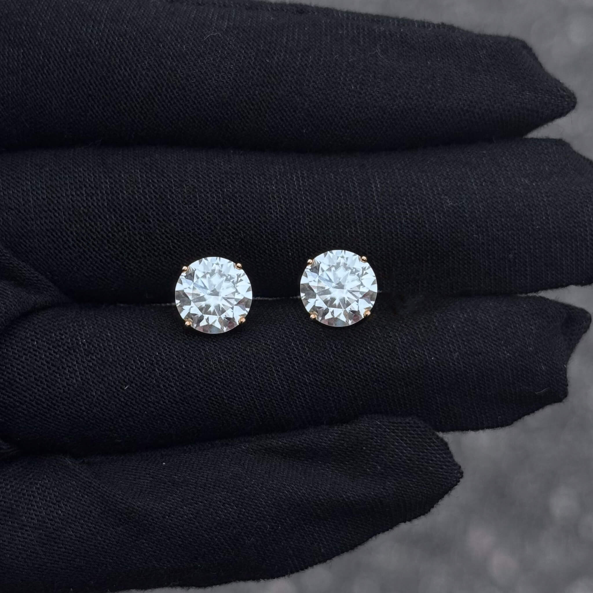 Close-up of 8mm round moissanite solitaire earrings showing 3.2ct stones held in prong setting on black glove.