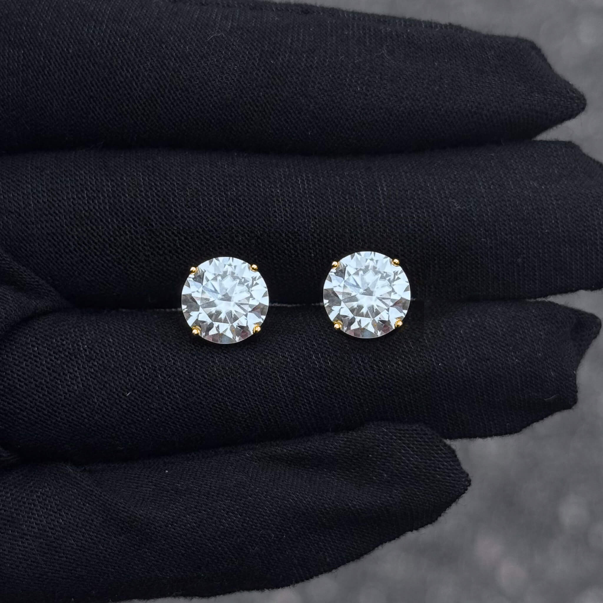 9mm moissanite stud earrings with round 6.2ct stones in gold prong setting displayed on black glove.