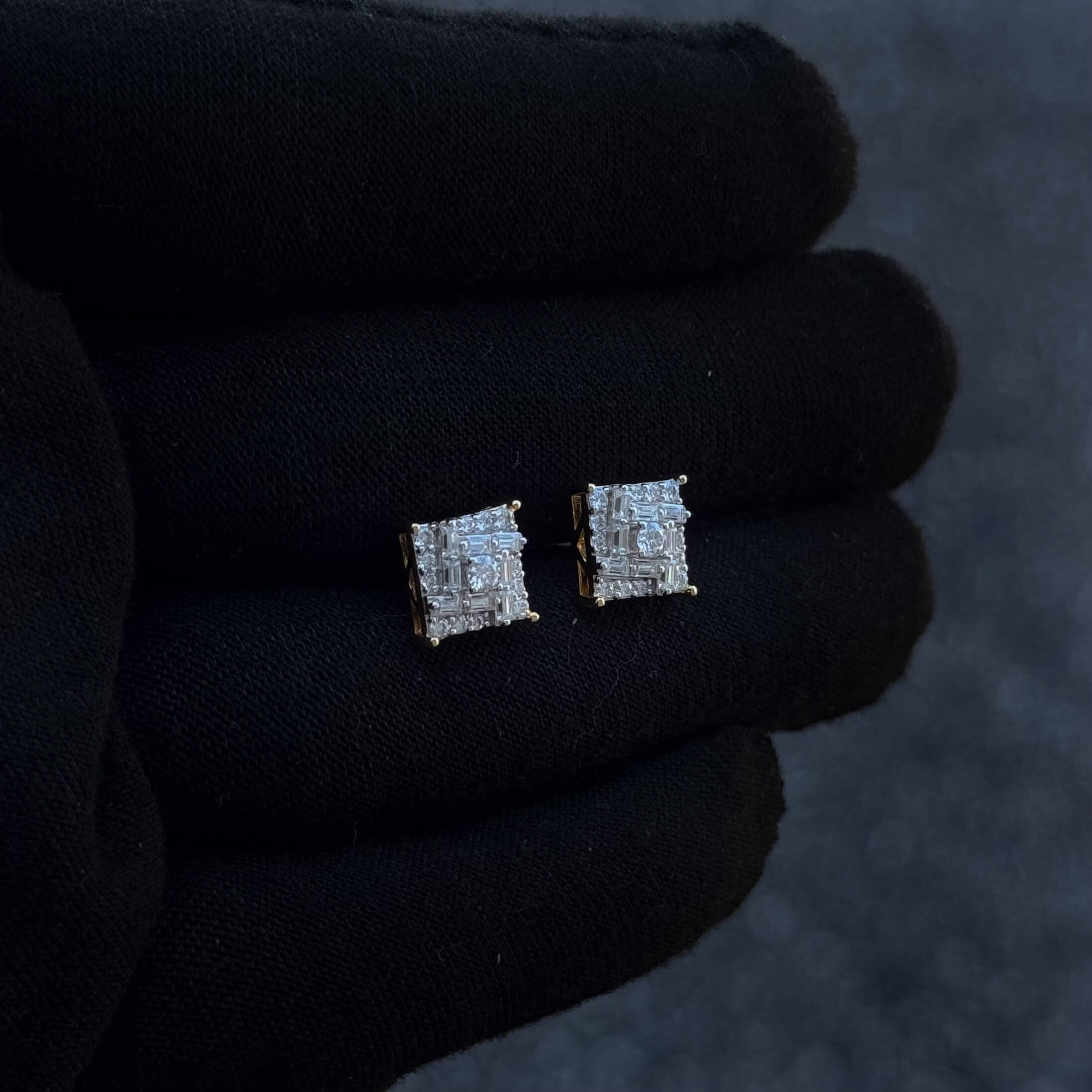 Side-angled view of 9mm square moissanite cluster earrings with gold prongs on black glove.