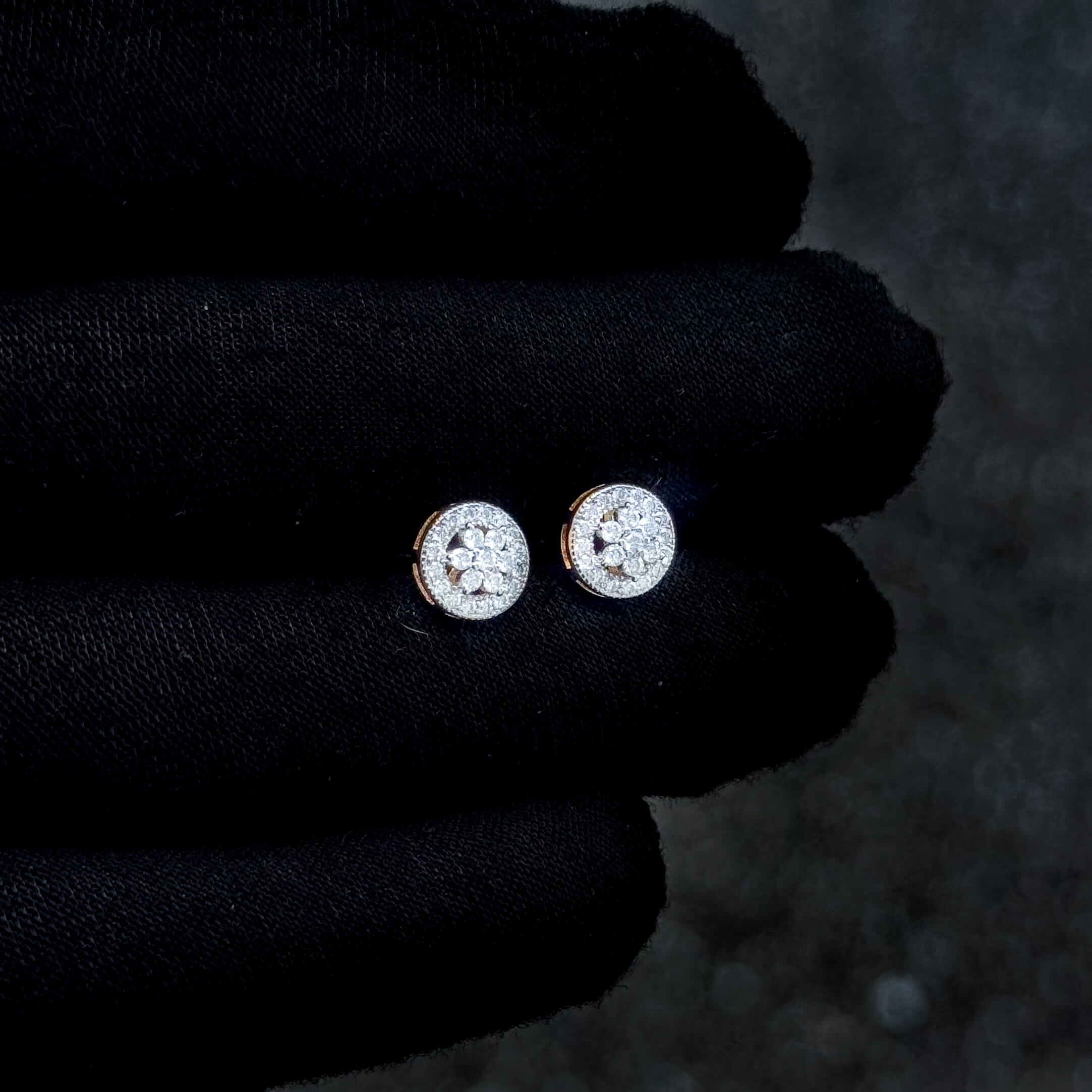 Round moissanite cluster earrings shown on black glove, featuring diamond halo and silver base.