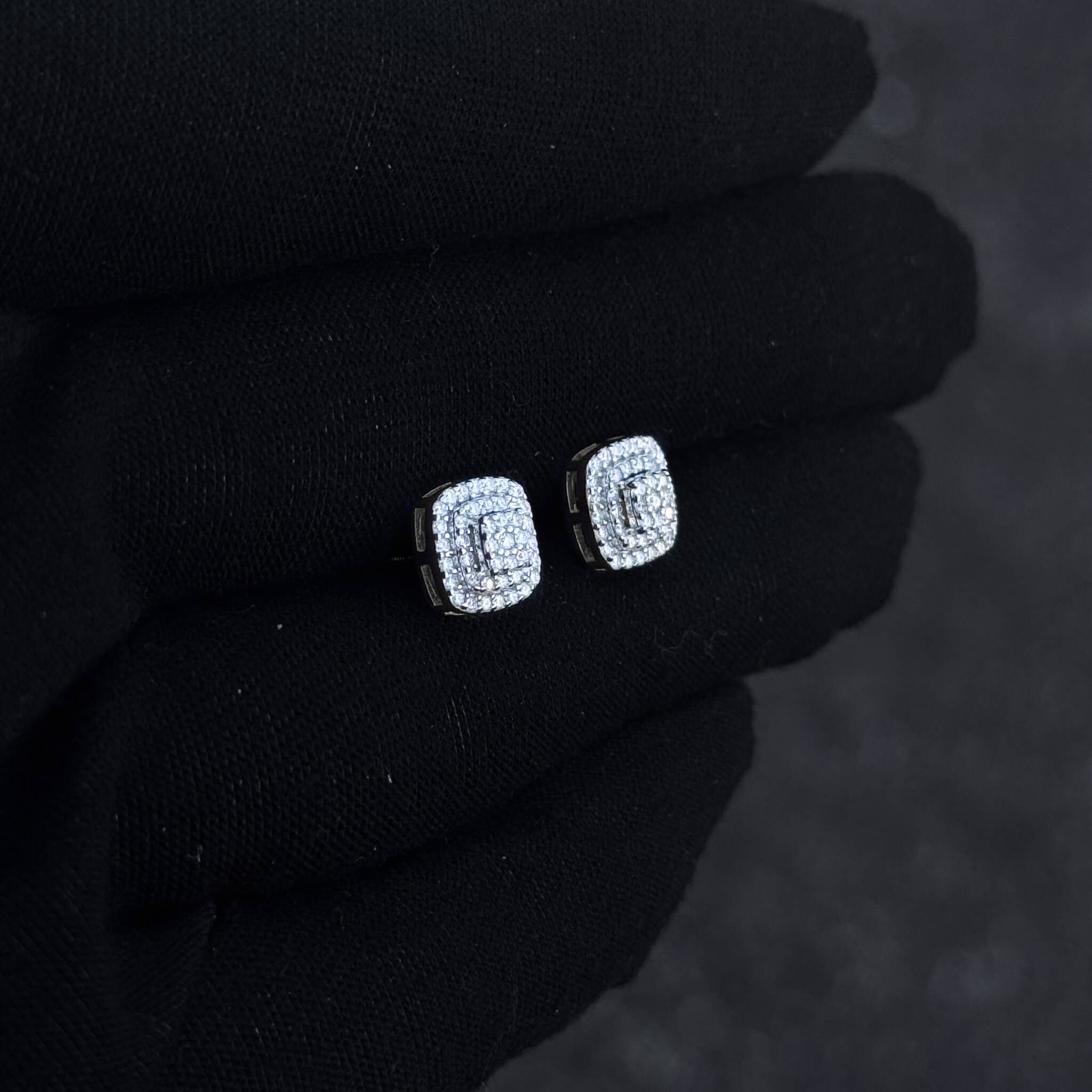 Silver-tone square moissanite cluster stud earrings with layered halo diamonds displayed on black glove.