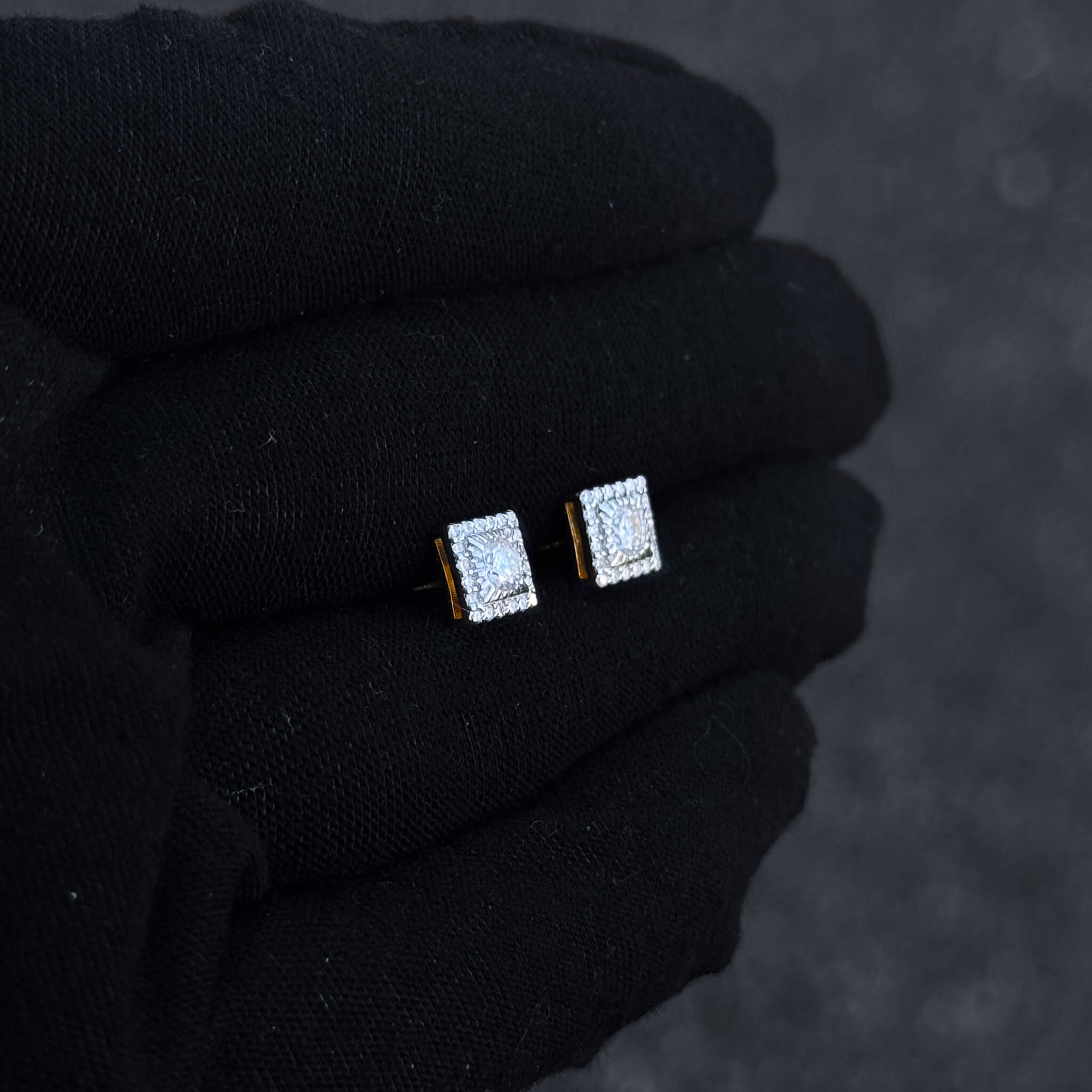 Angled view of square moissanite cluster earrings with gold side detail shown on black glove.