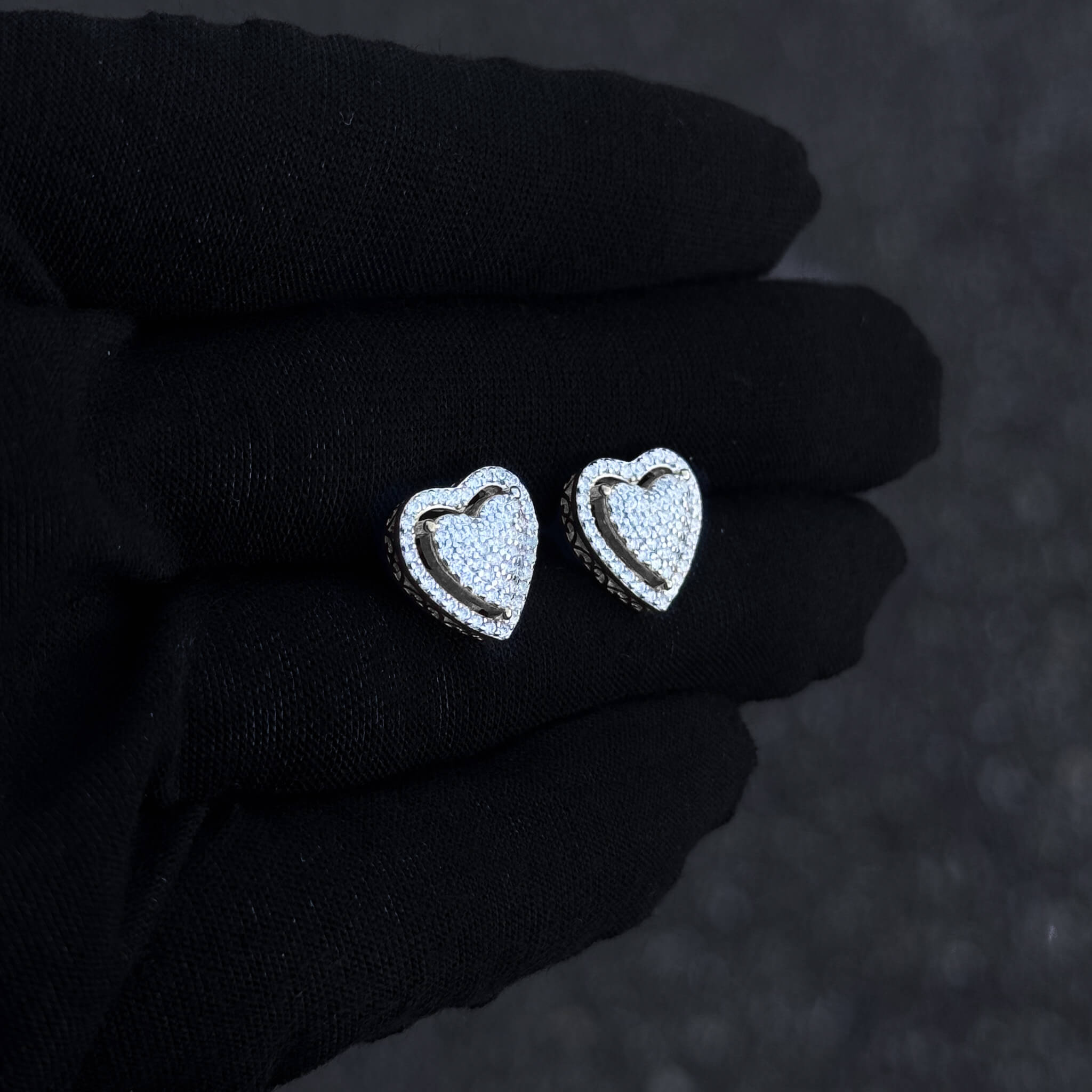 Sterling silver heart moissanite cluster earrings displayed on black glove in soft lighting.