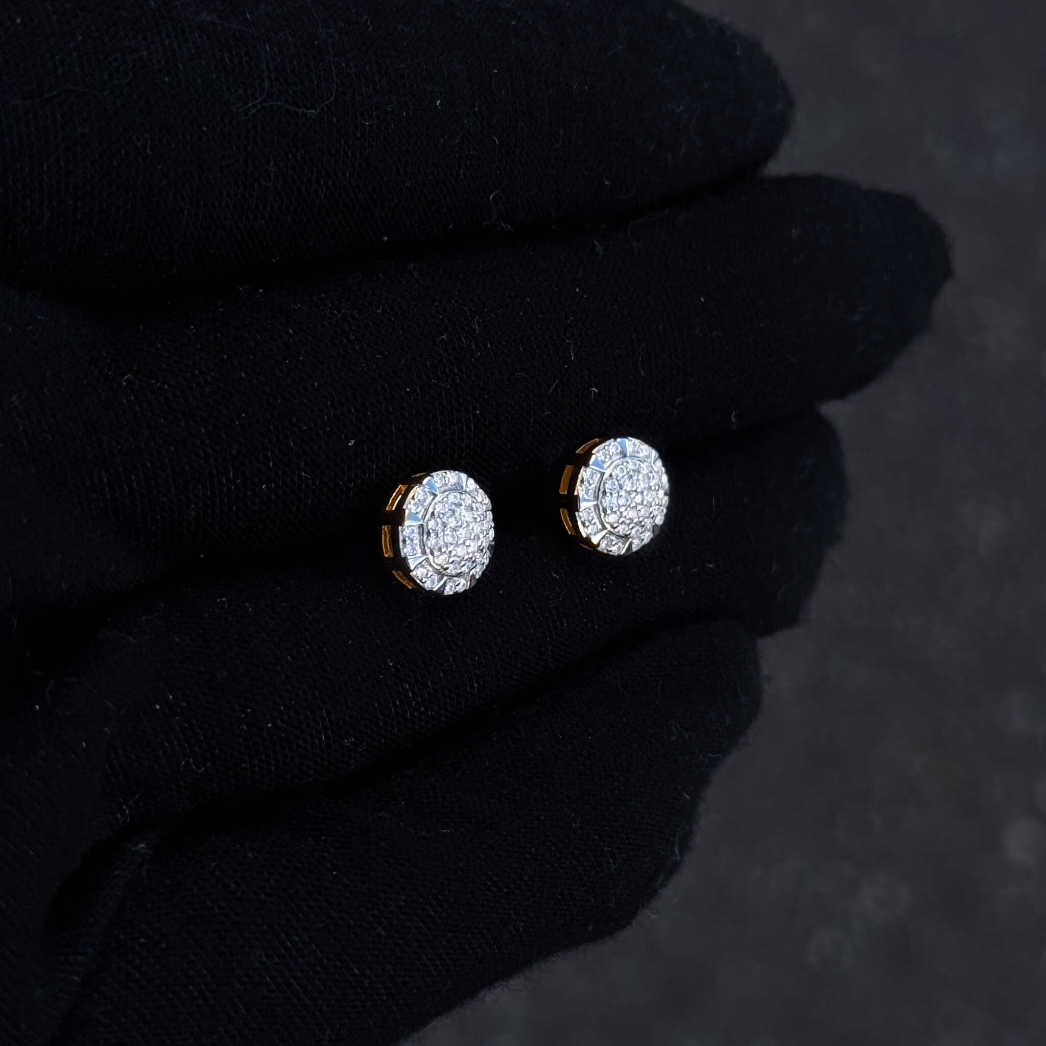 Round moissanite cluster earrings with gold-trim sides displayed on black glove in soft light.