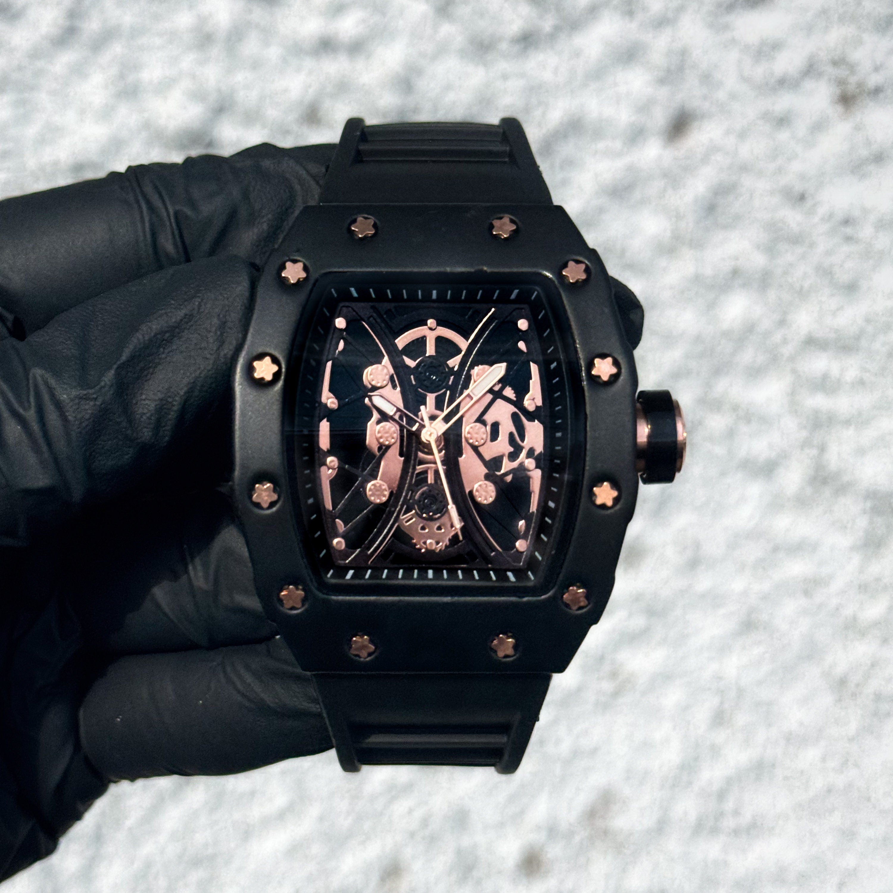 Men’s 42mm black tonneau watch with rose gold skeleton dial details and matte case with silicone band.