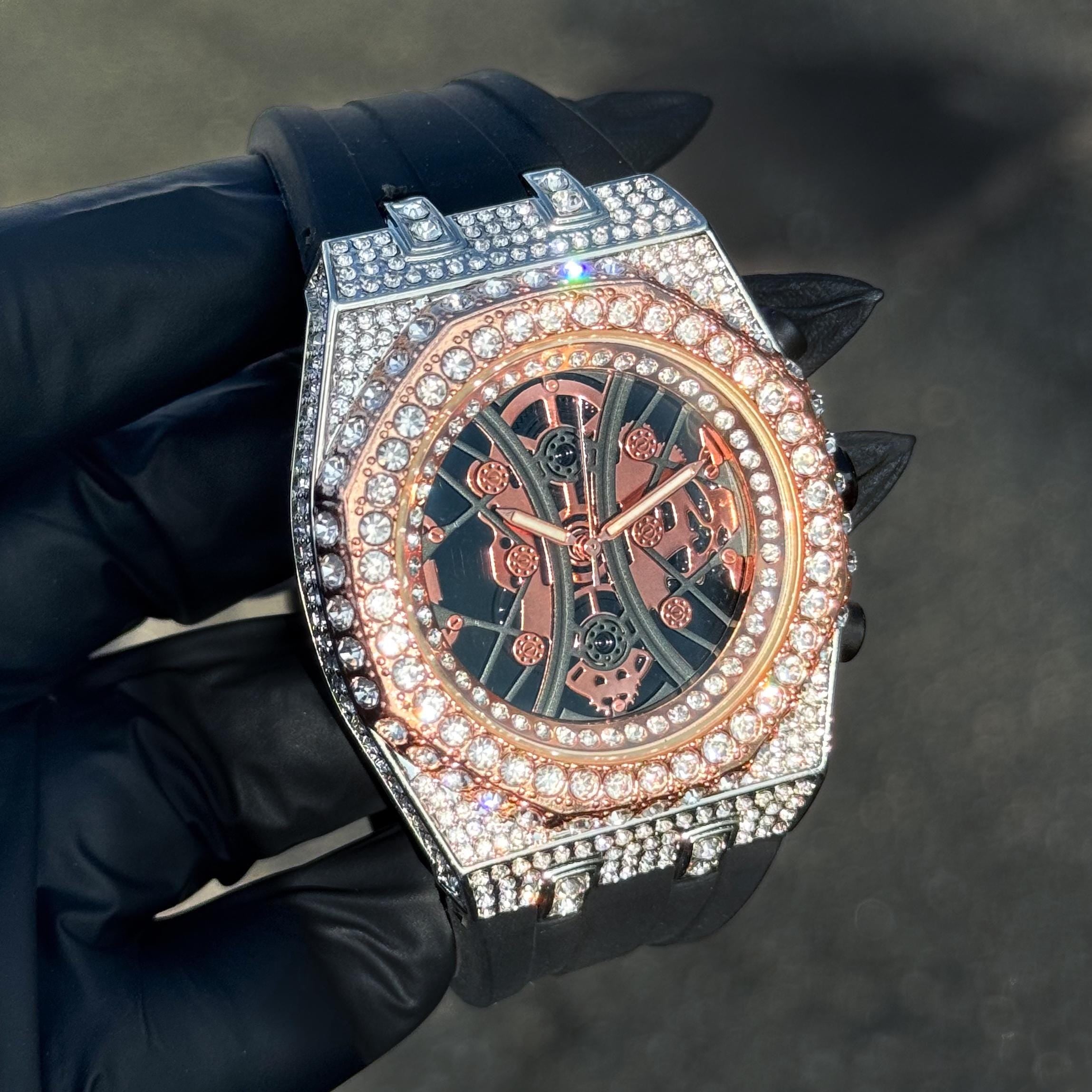 Rose gold Men’s 43mm iced octagon bezel watch with skeleton dial and black band.