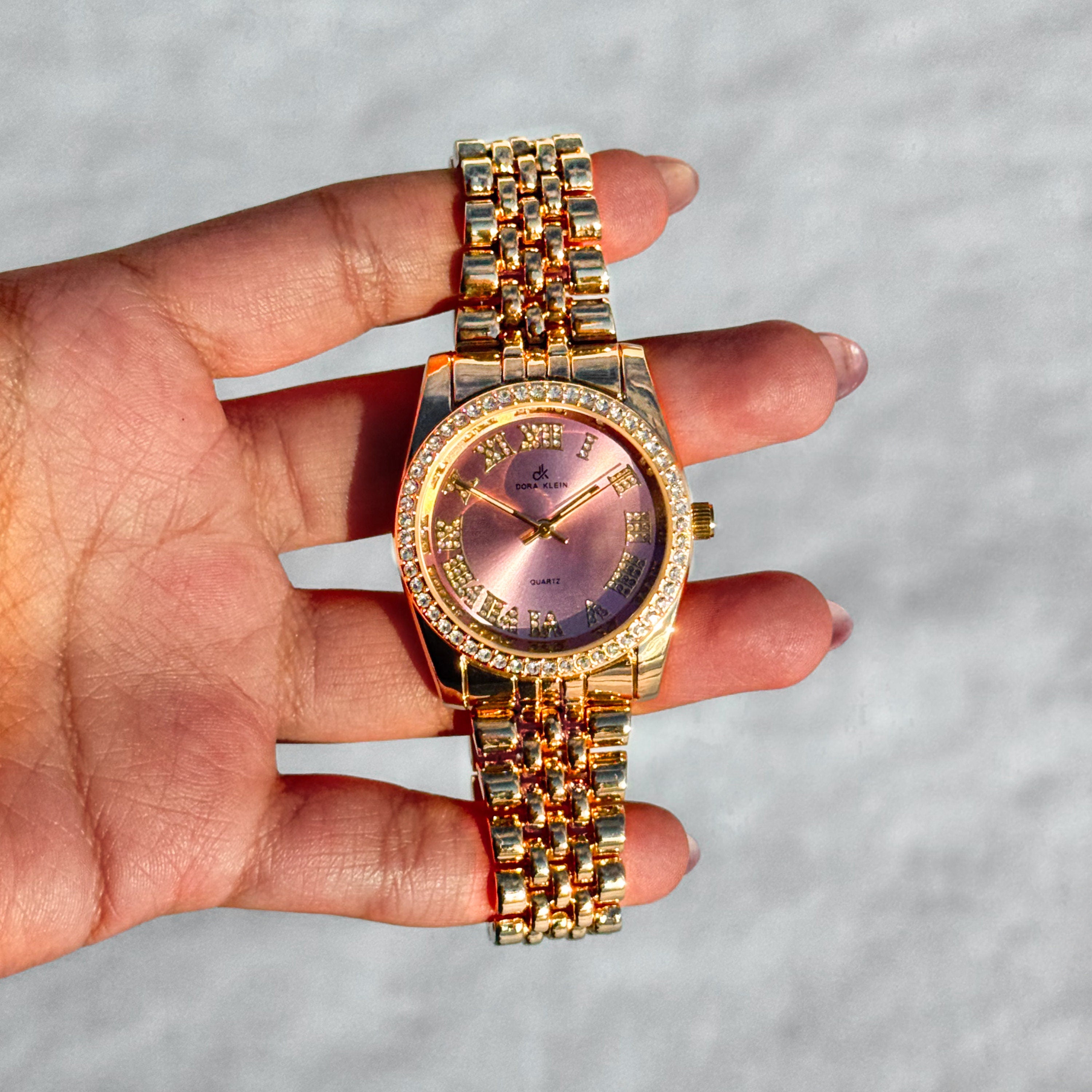Gold Women's 35mm Roman dial watch with pink face and diamond-studded bezel, quartz movement.