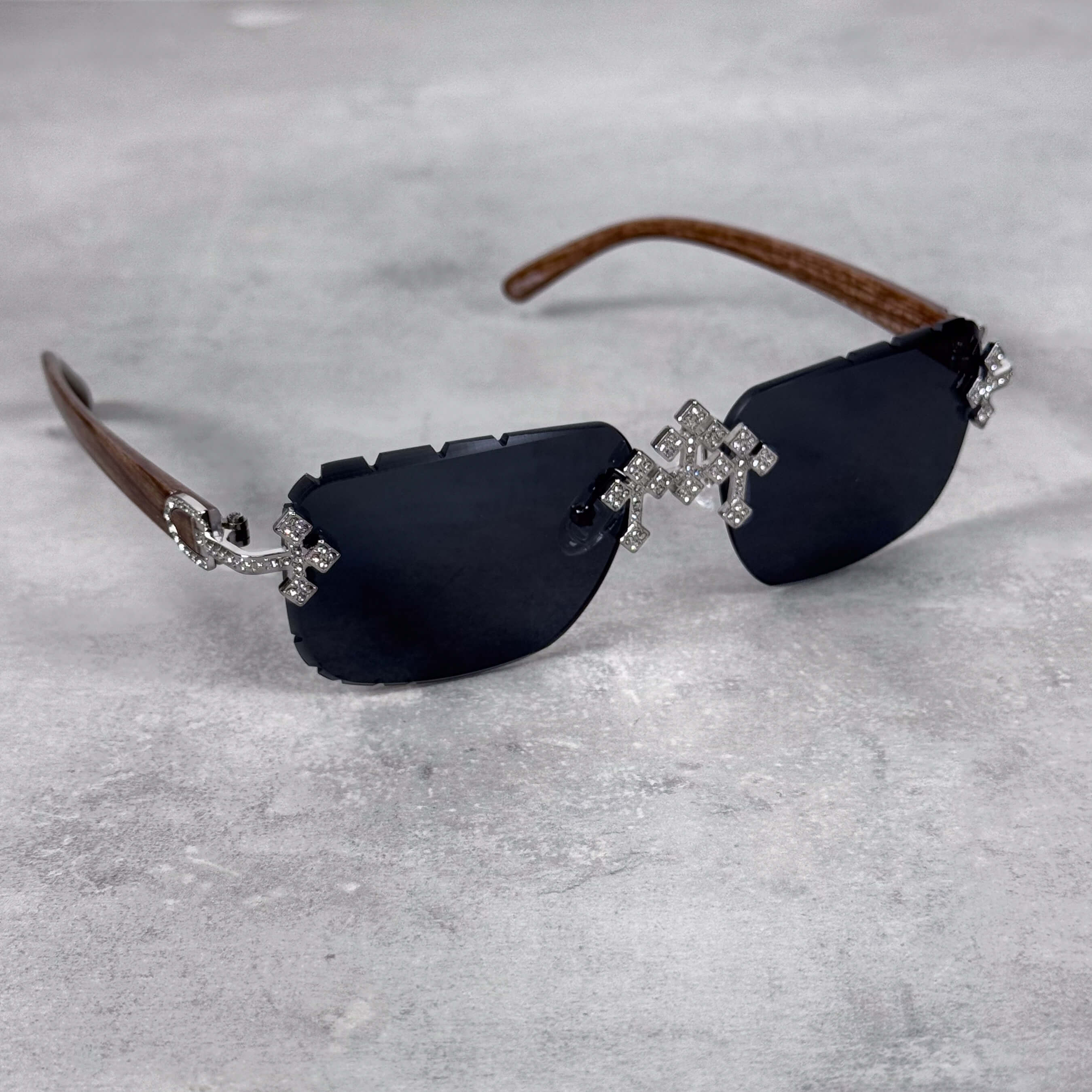 Black-lens rimless sunglasses with iced triple cross detailing and brown wooden-style arms.