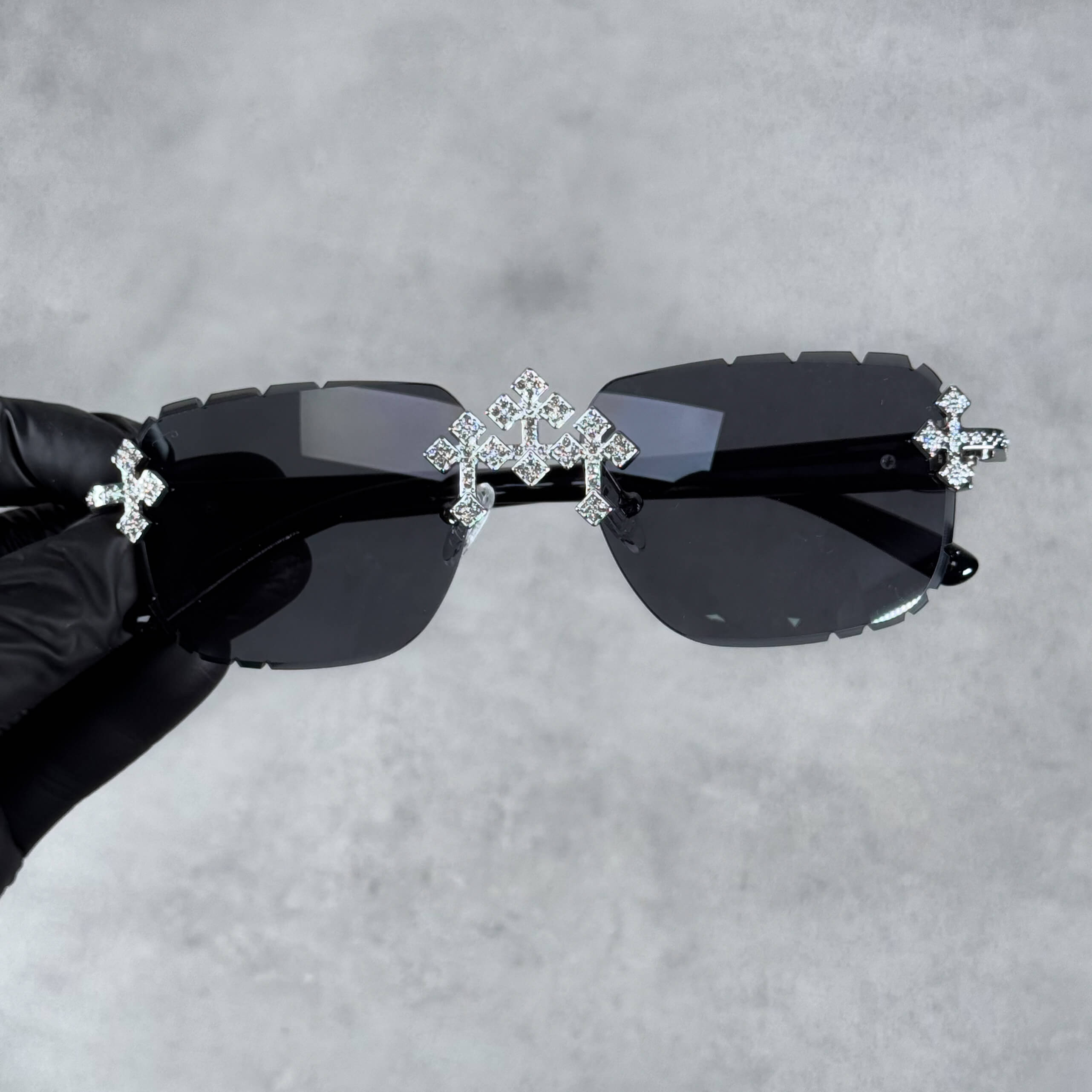 Iced triple cross sunglasses with dark black lenses and shimmering silver cross embellishments.