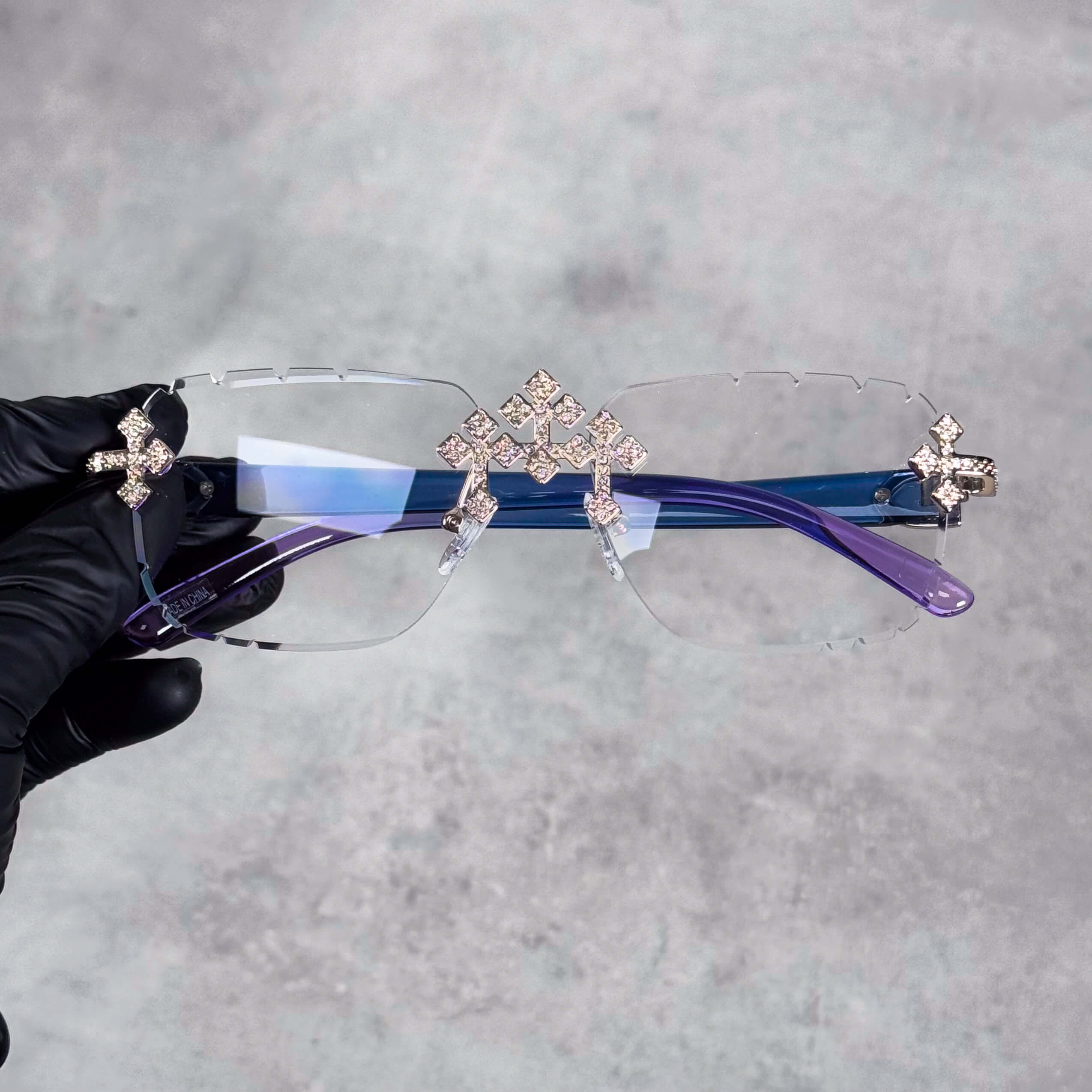 Rimless clear Iced Triple Cross Sunglasses with gold crystal crosses and blue-purple temples.