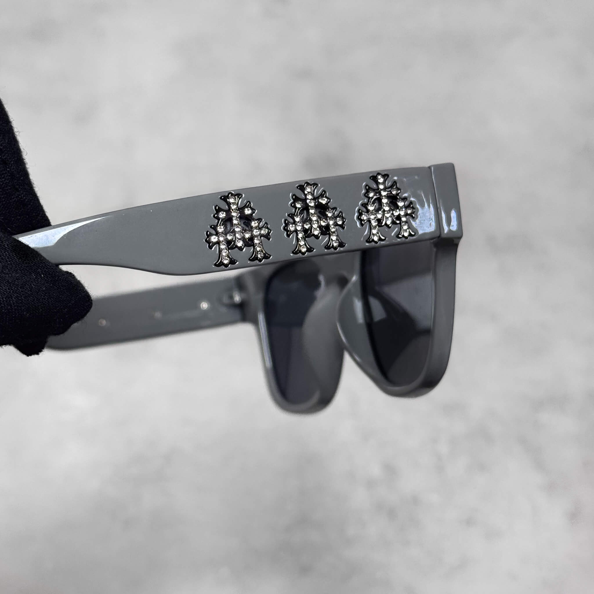 Close-up of grey Triple Cross Chrome Inspired Sunglasses featuring three cross emblems on arms.