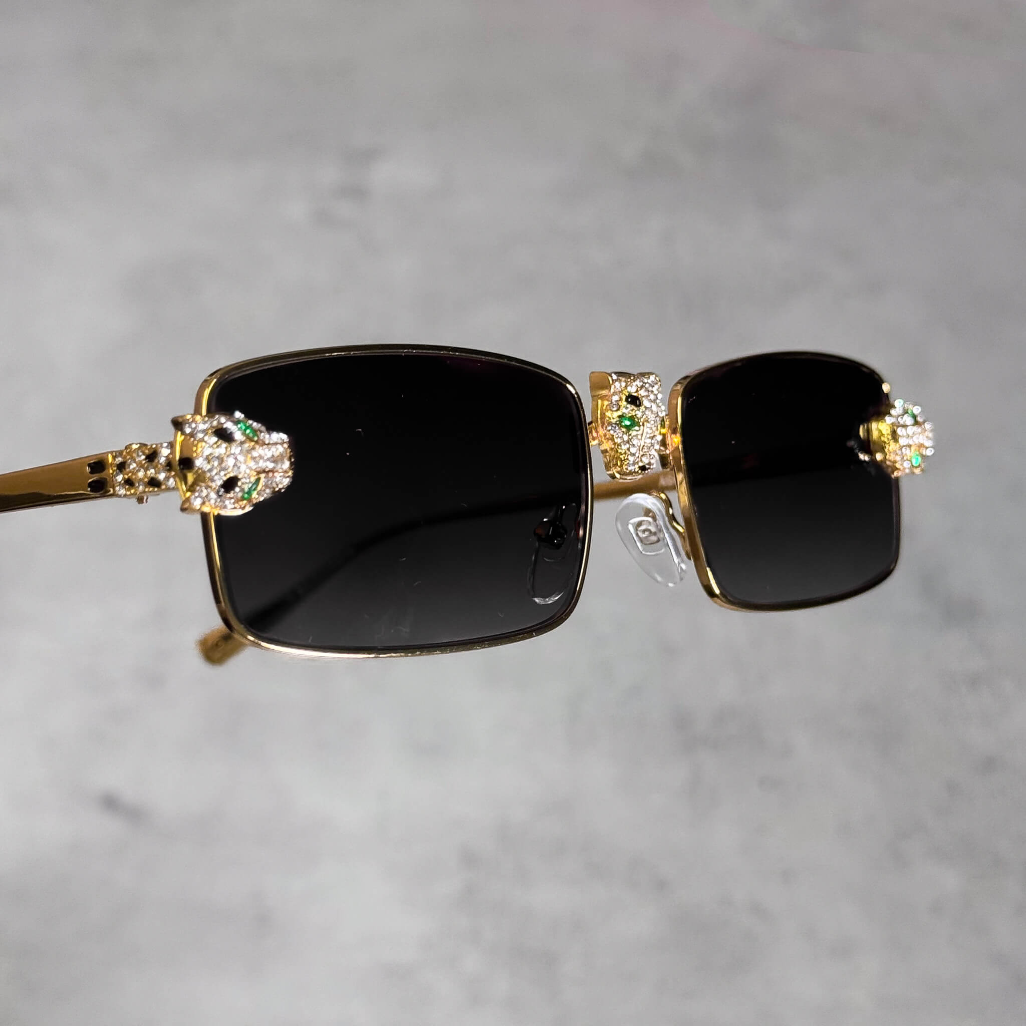 Gold rectangular black-lens sunglasses featuring iced-out panther heads and luxury detailing.