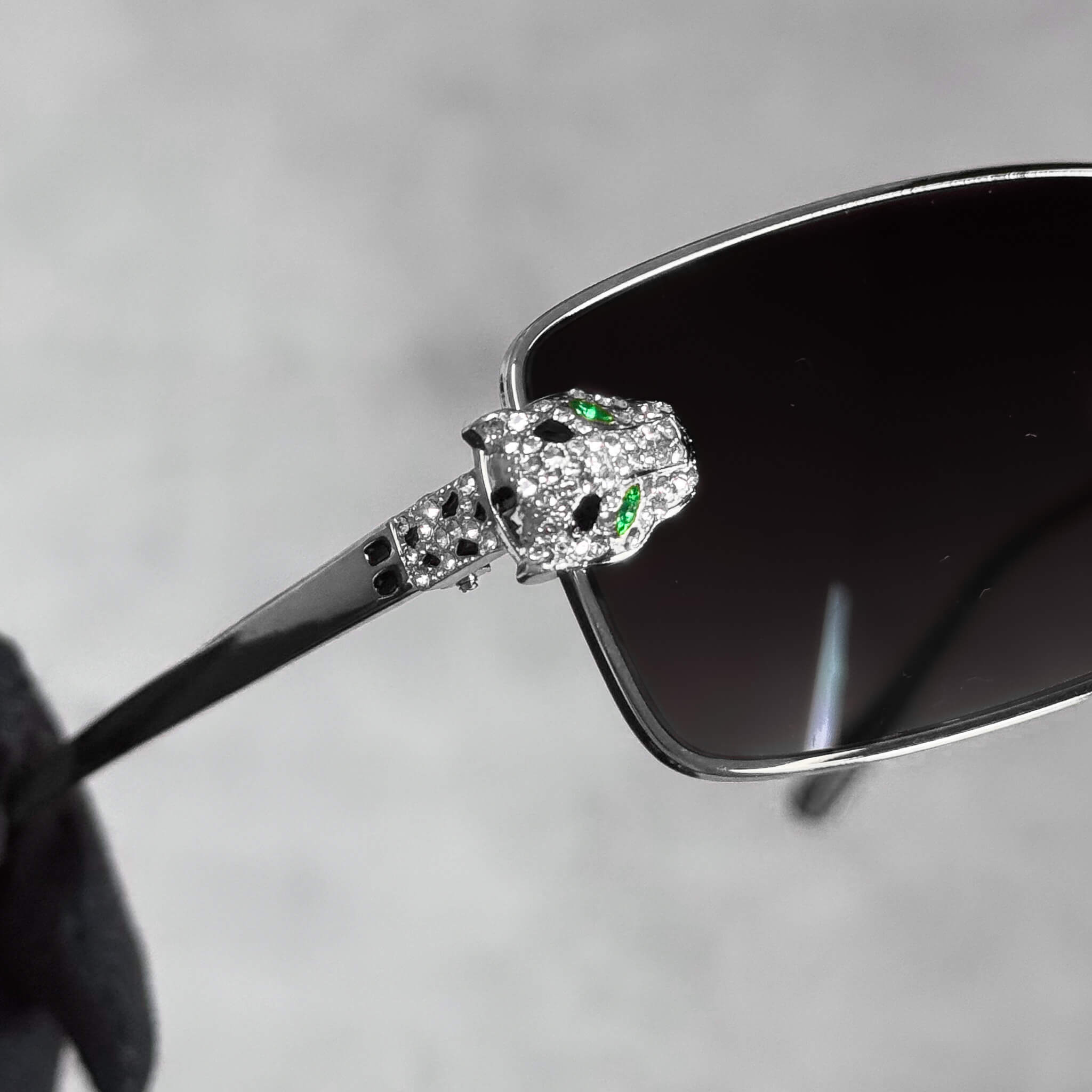 Close-up of silver Iced Out Panther Sunglasses showing crystal panther head with green stones.