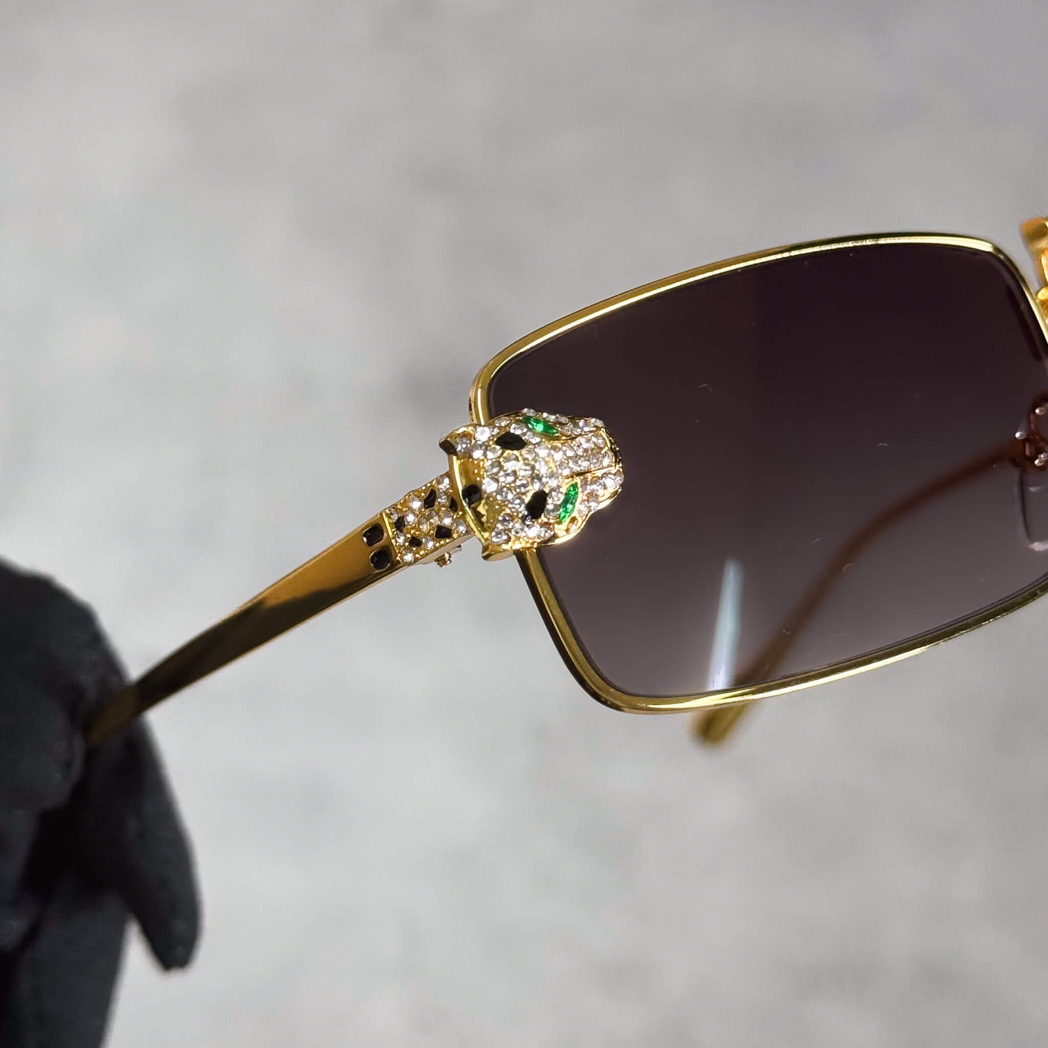Close-up of gold Iced Out Panther Sunglasses showing jeweled panther head with green stones.