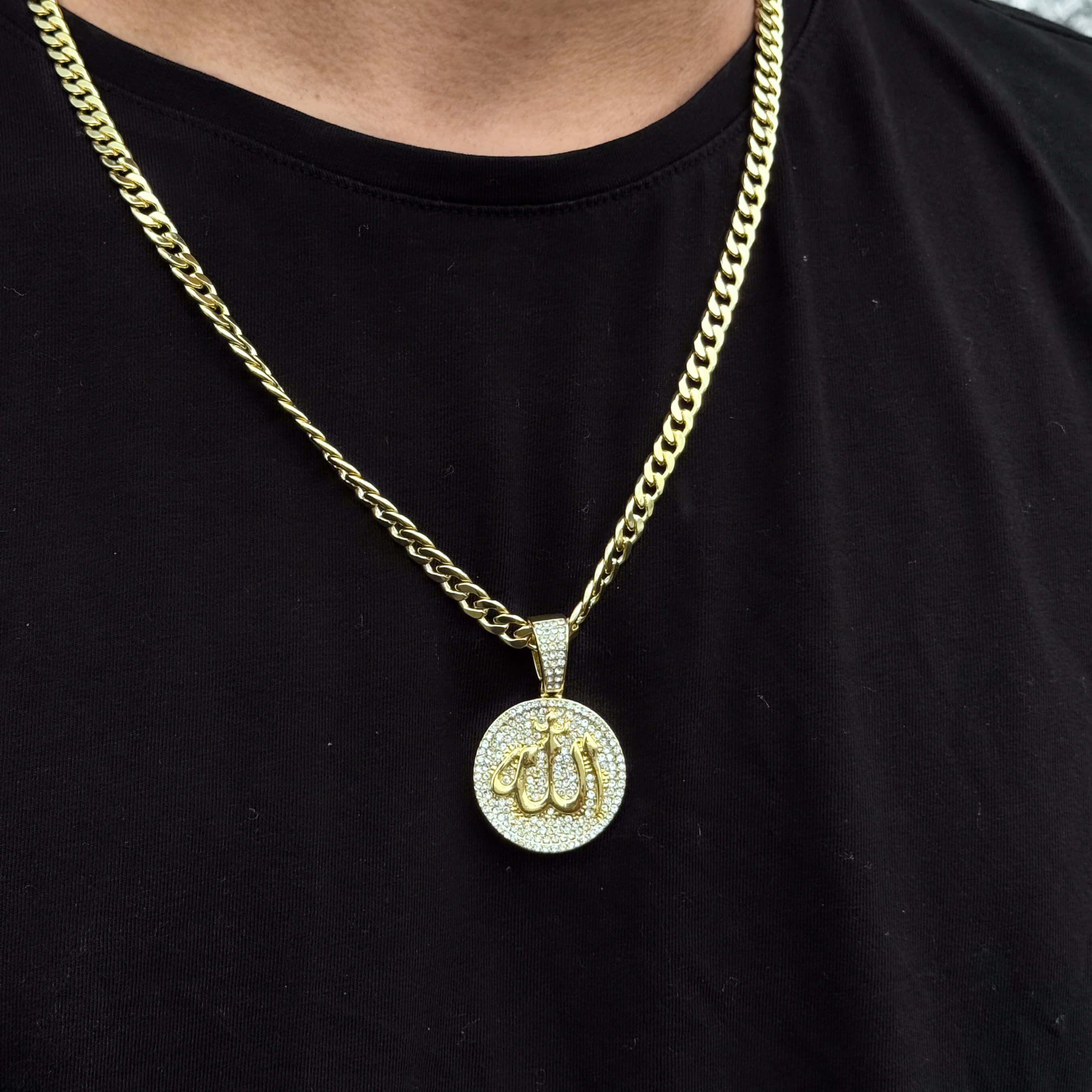 Gold iced-out round Allah medallion pendant on 6mm Cuban chain shown worn on black tee.