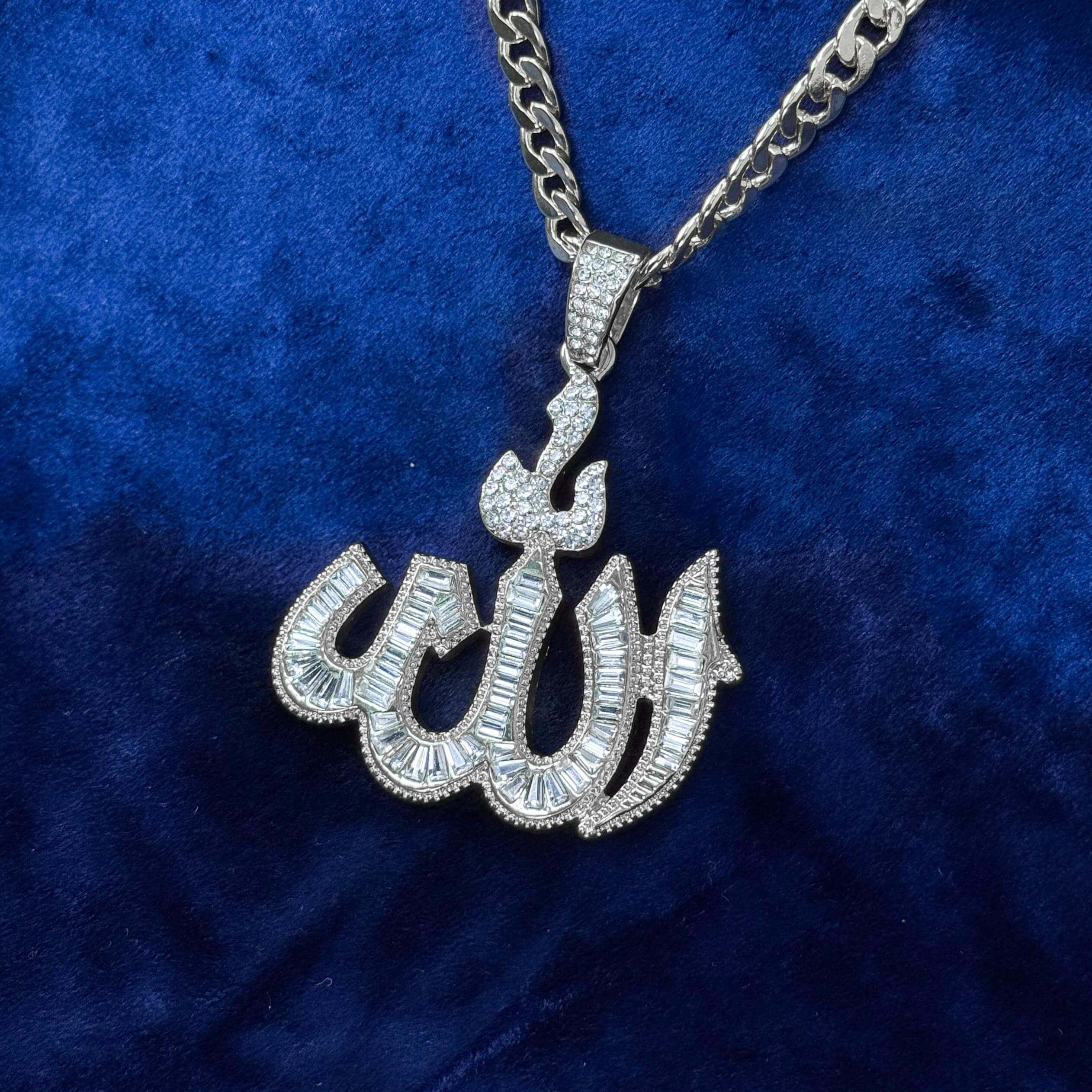 Silver iced-out baguette Allah pendant with Cuban chain displayed on velvet surface for clarity.