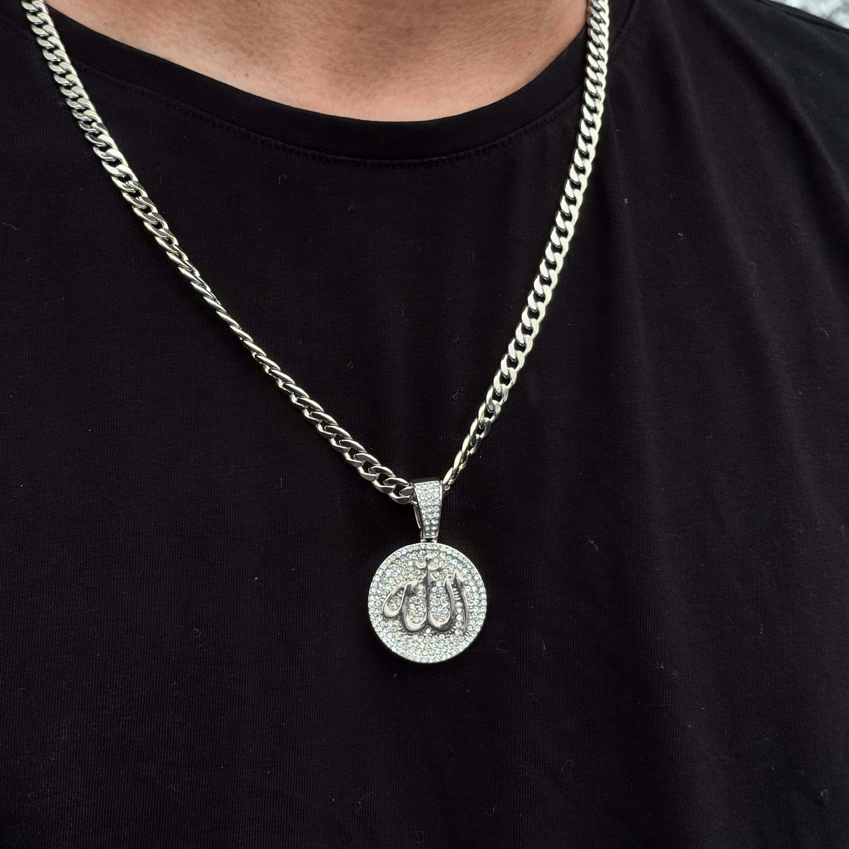 Silver round iced-out Allah medallion pendant worn with 6mm Cuban chain on black tee.