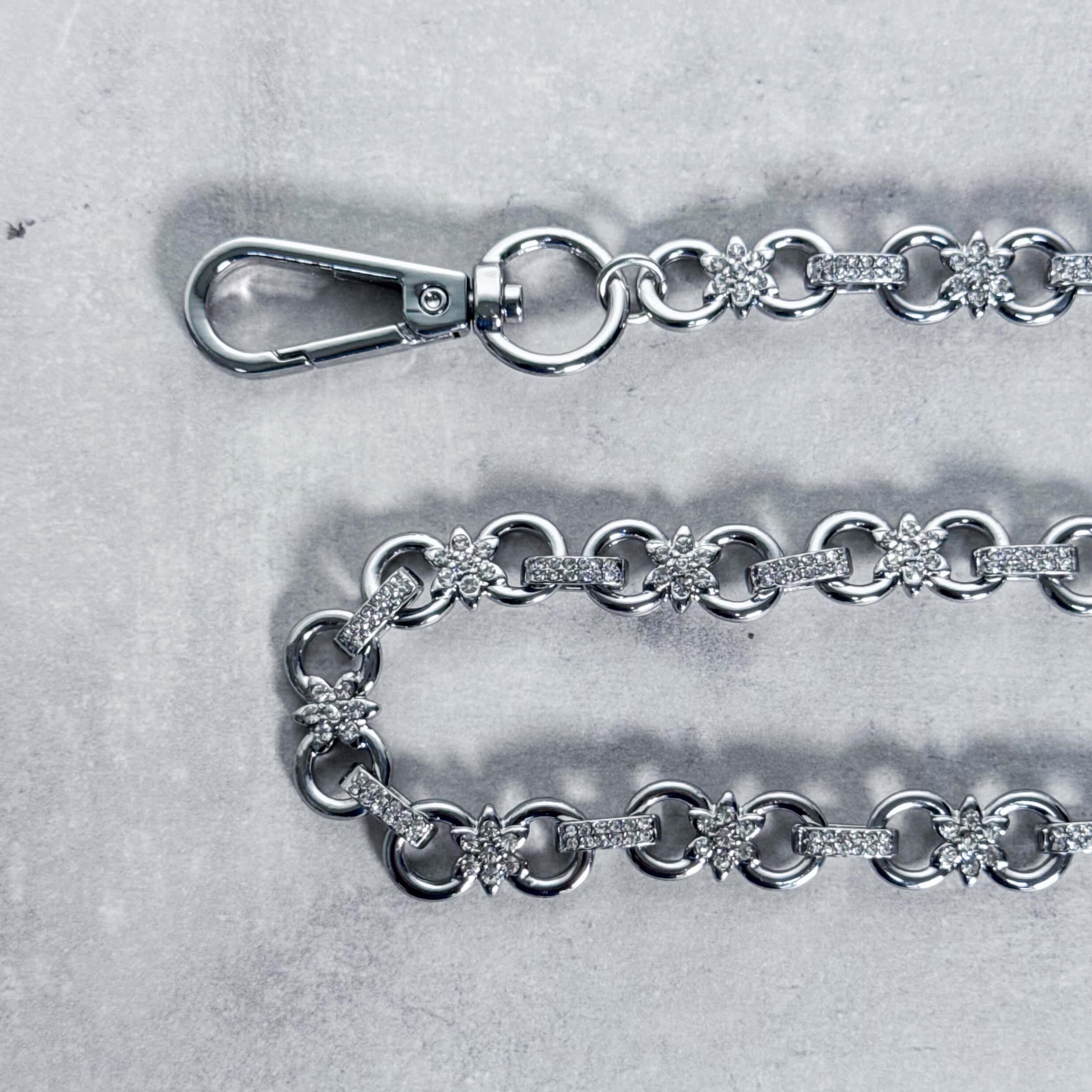 Close-up of Iced Out Flower Infinity Link Pant Chain highlighting crystal flower connectors and textured links.