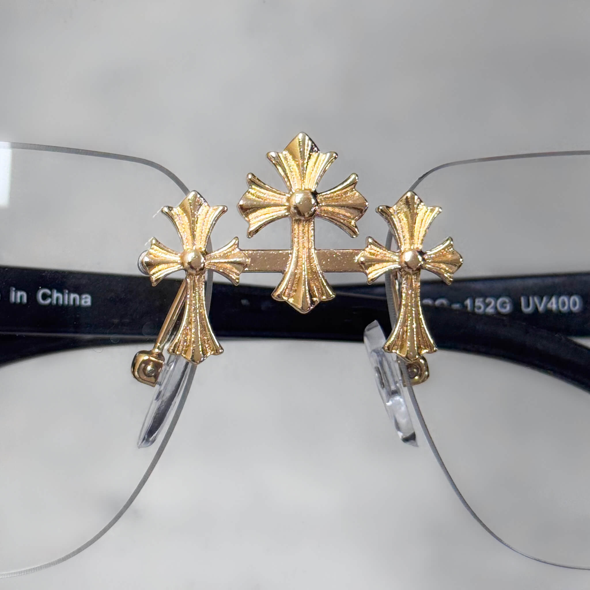 Gold triple-cross detail on clear-lens Solid Triple Cross Sunglasses with black frame.