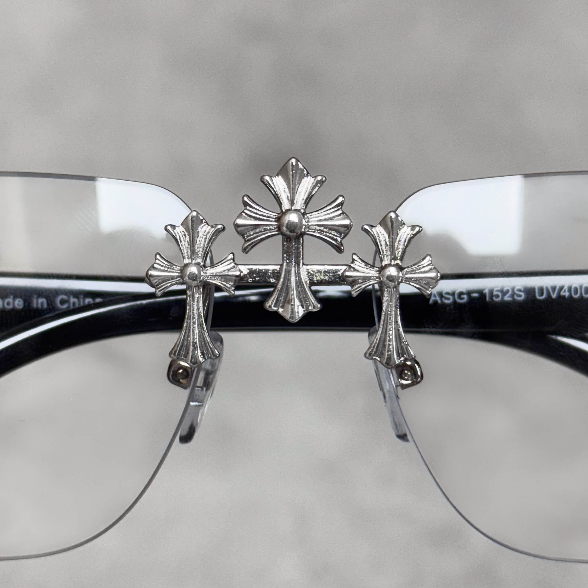 Silver triple-cross embellishment on clear-lens Solid Triple Cross Sunglasses rimless frame.