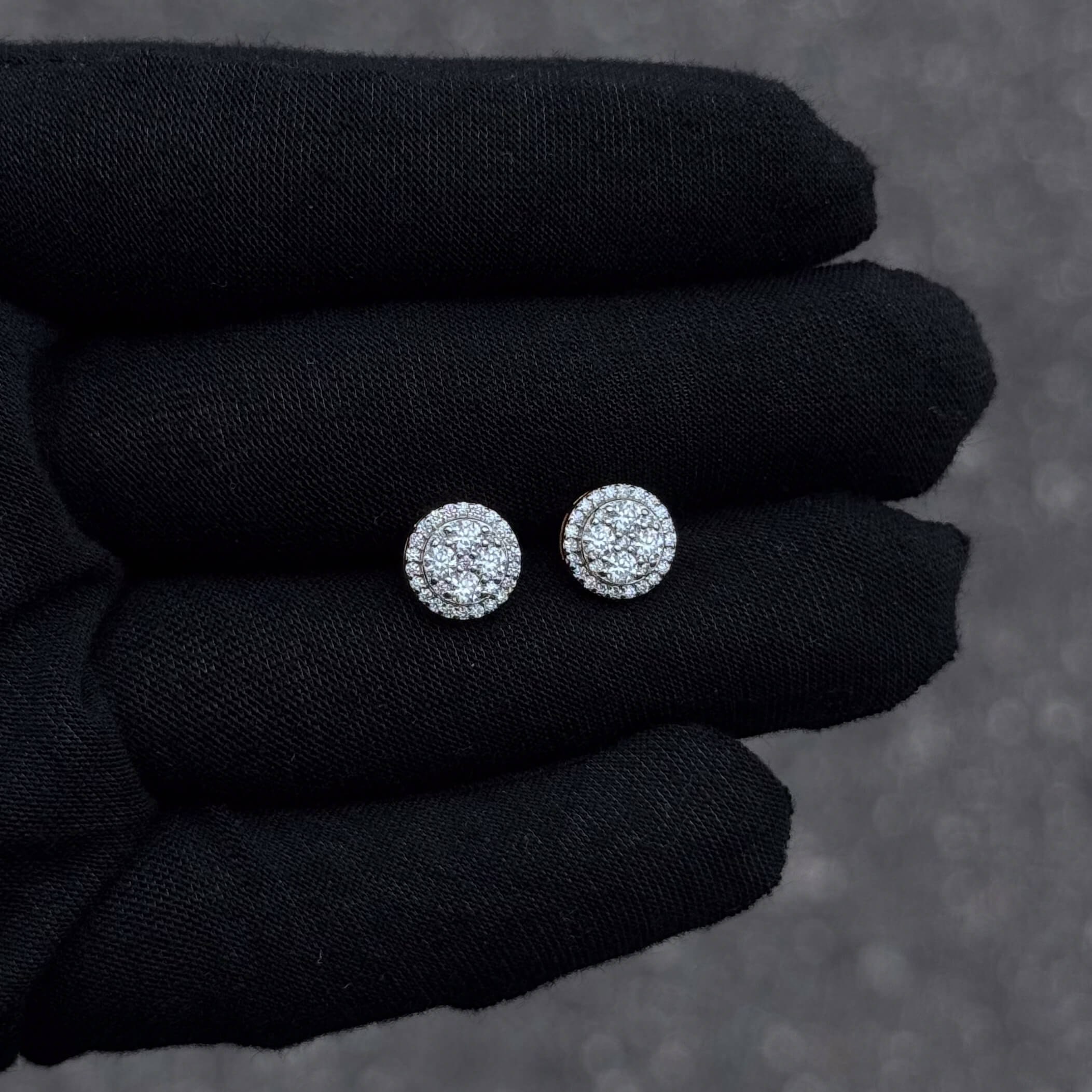 Hand-held view of 9mm round moissanite cluster earrings in sterling silver with halo detail.