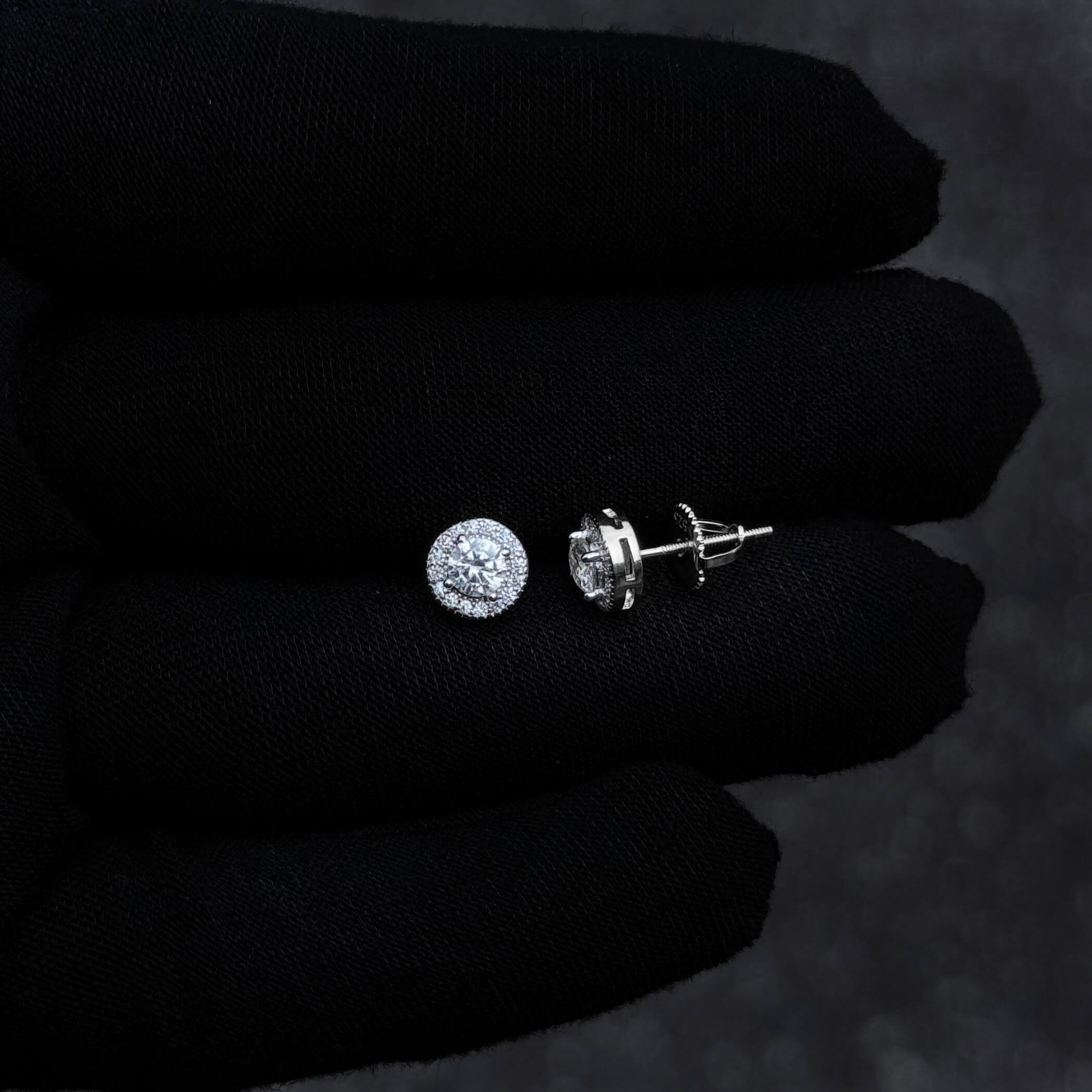 Silver moissanite halo stud earrings with screw-back posts shown on black glove.