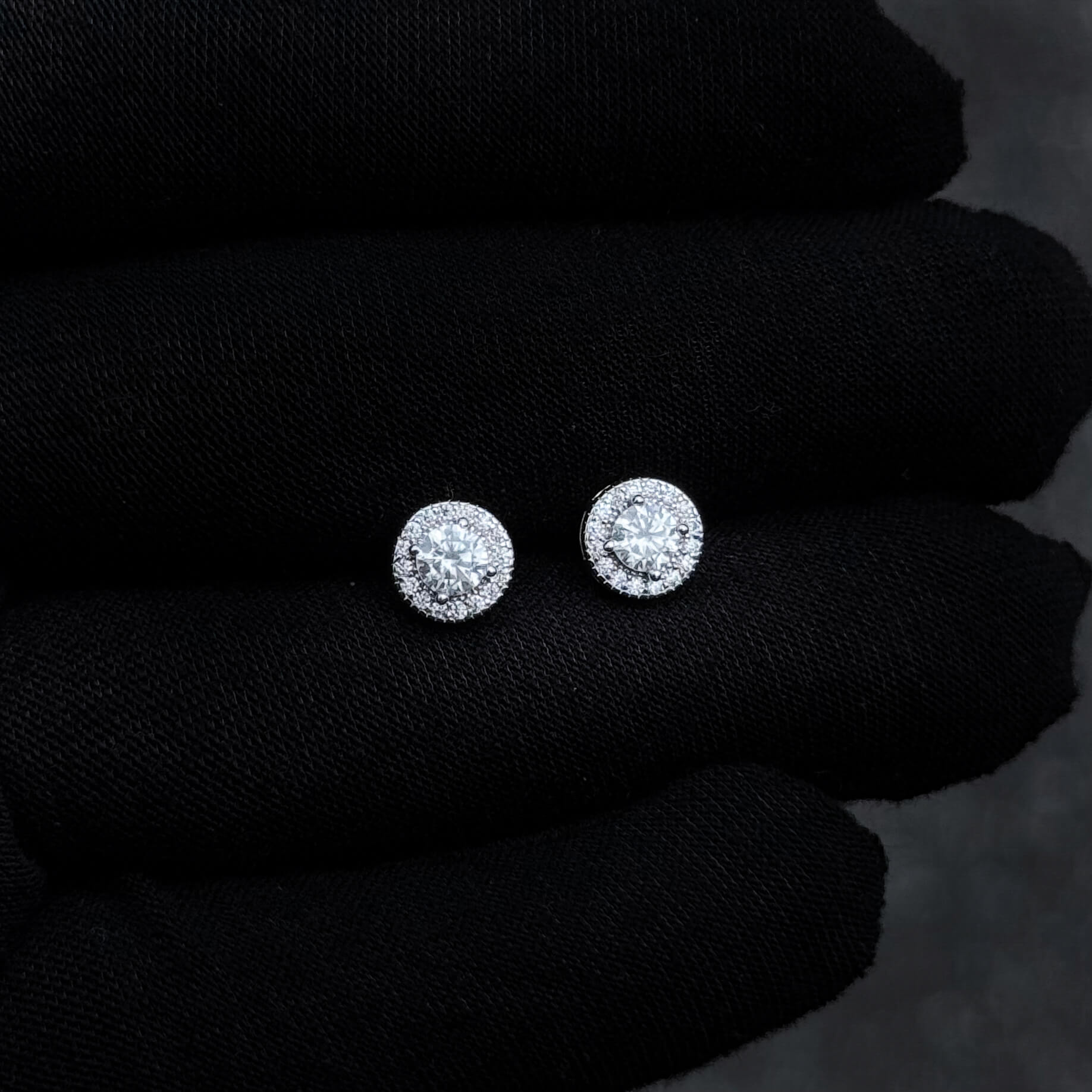 Silver moissanite diamond halo stud earrings displayed on black glove background.