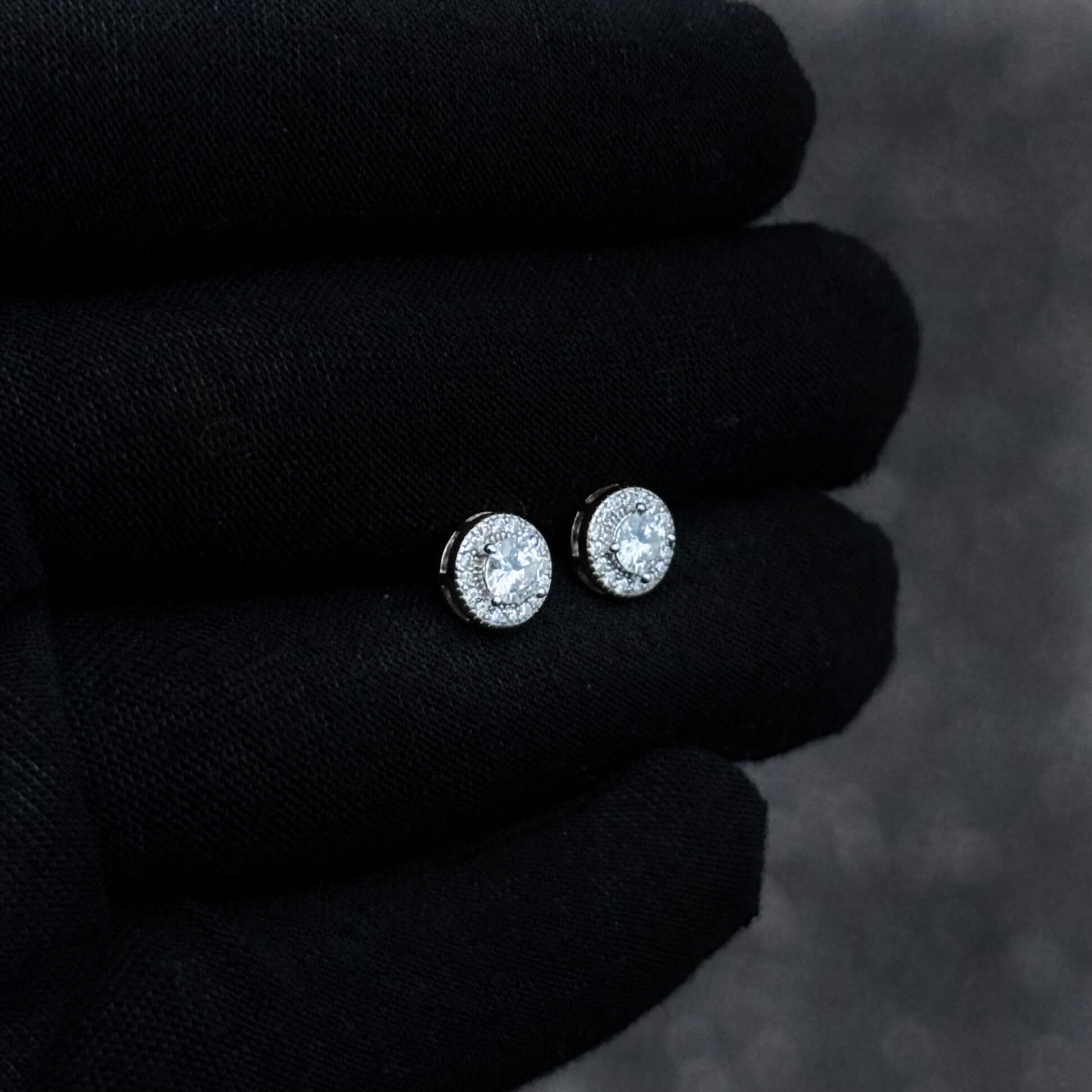 Small round moissanite cluster diamond studs in silver shown on black glove.