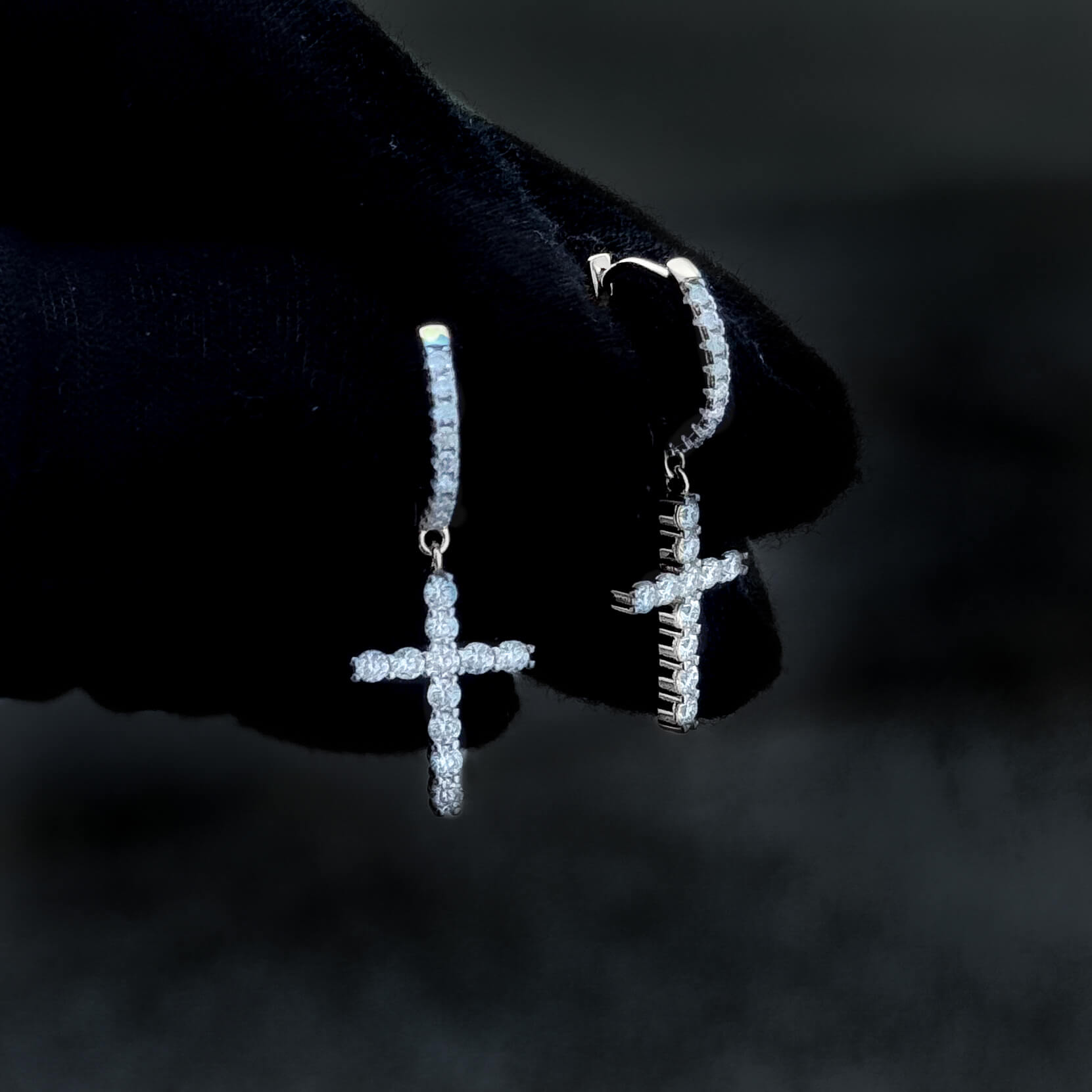 Sterling silver moissanite cross drop earrings with round diamond clusters held on gloved hand.