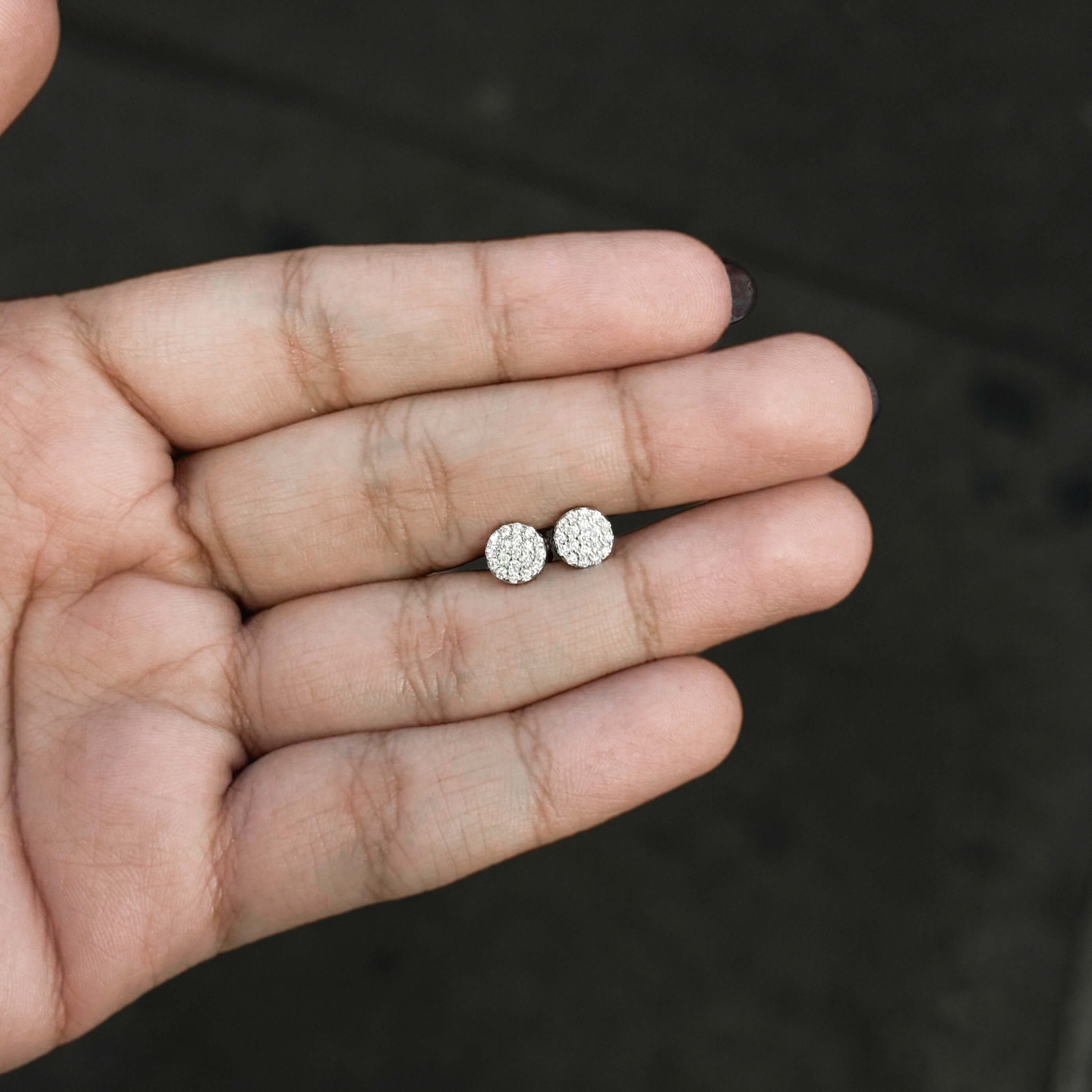 Small round moissanite cluster stud earrings shown in hand, sparkly pavé sterling silver design.