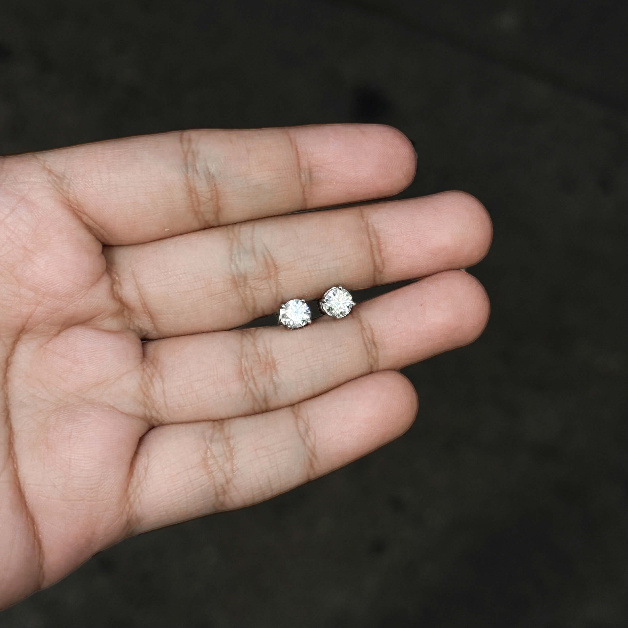 Small 5mm sterling silver Moissanite solitaire stud earrings shown resting on an open hand.