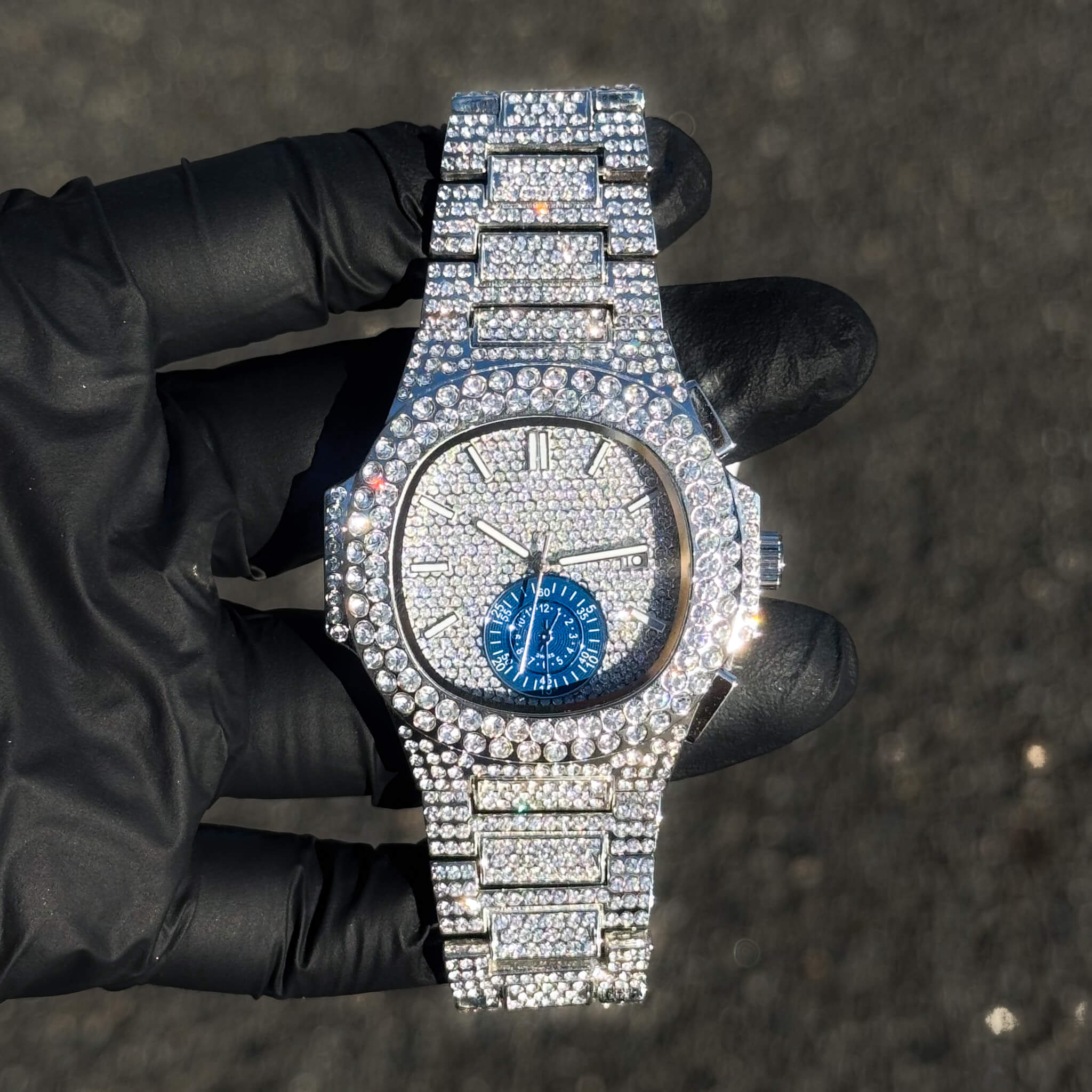 Men's 43mm silver iced-out diamond watch with blue subdial and fully crystal-set design.