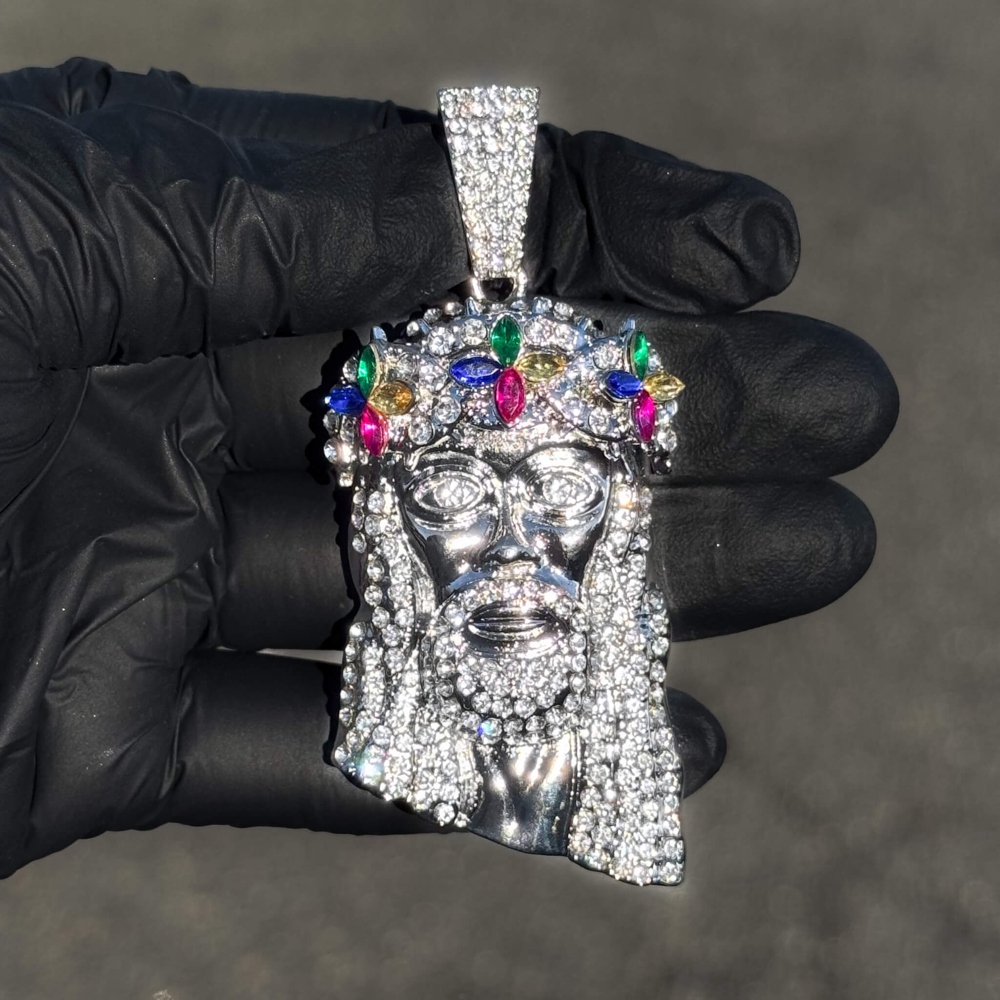Silver iced-out Jesus floral crown pendant with multicolor gemstones shown close-up in hand.