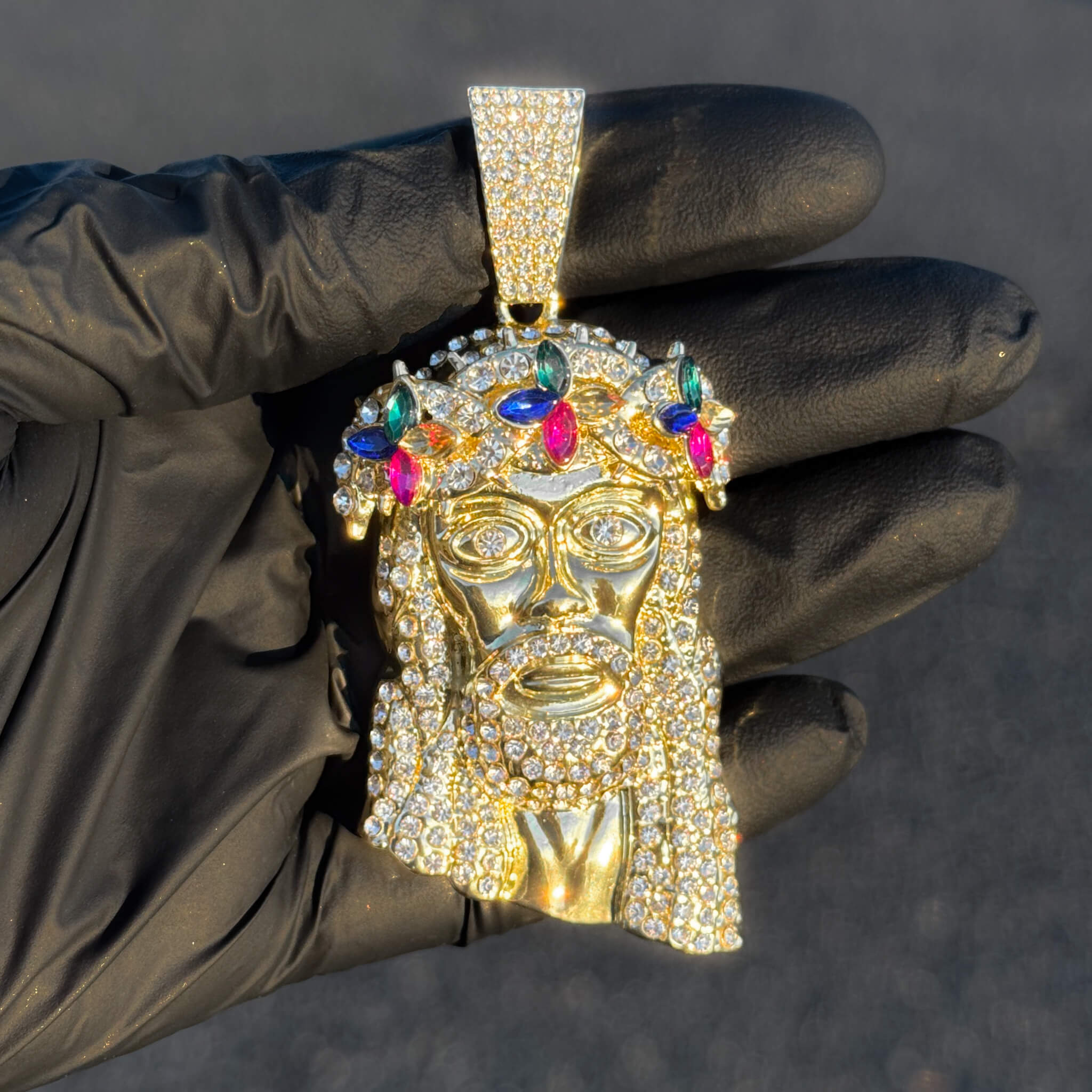Gold iced-out Jesus floral crown pendant featuring multicolor gemstones shown in hand.