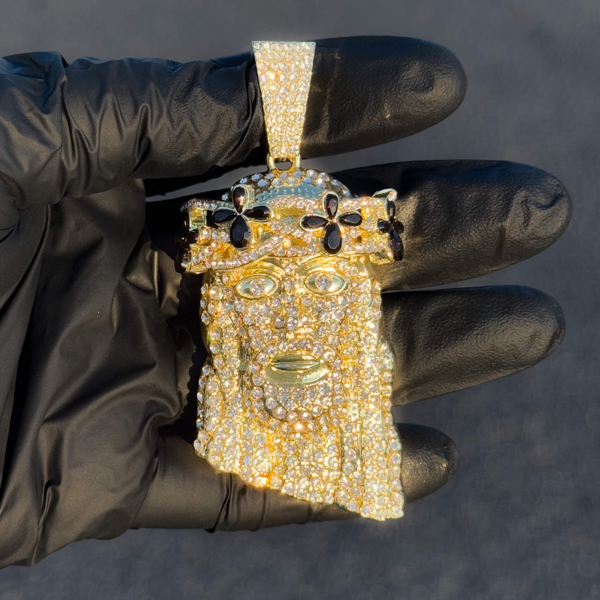 Gold iced-out Jesus pendant with black floral gemstones displayed in glove for close detailing.