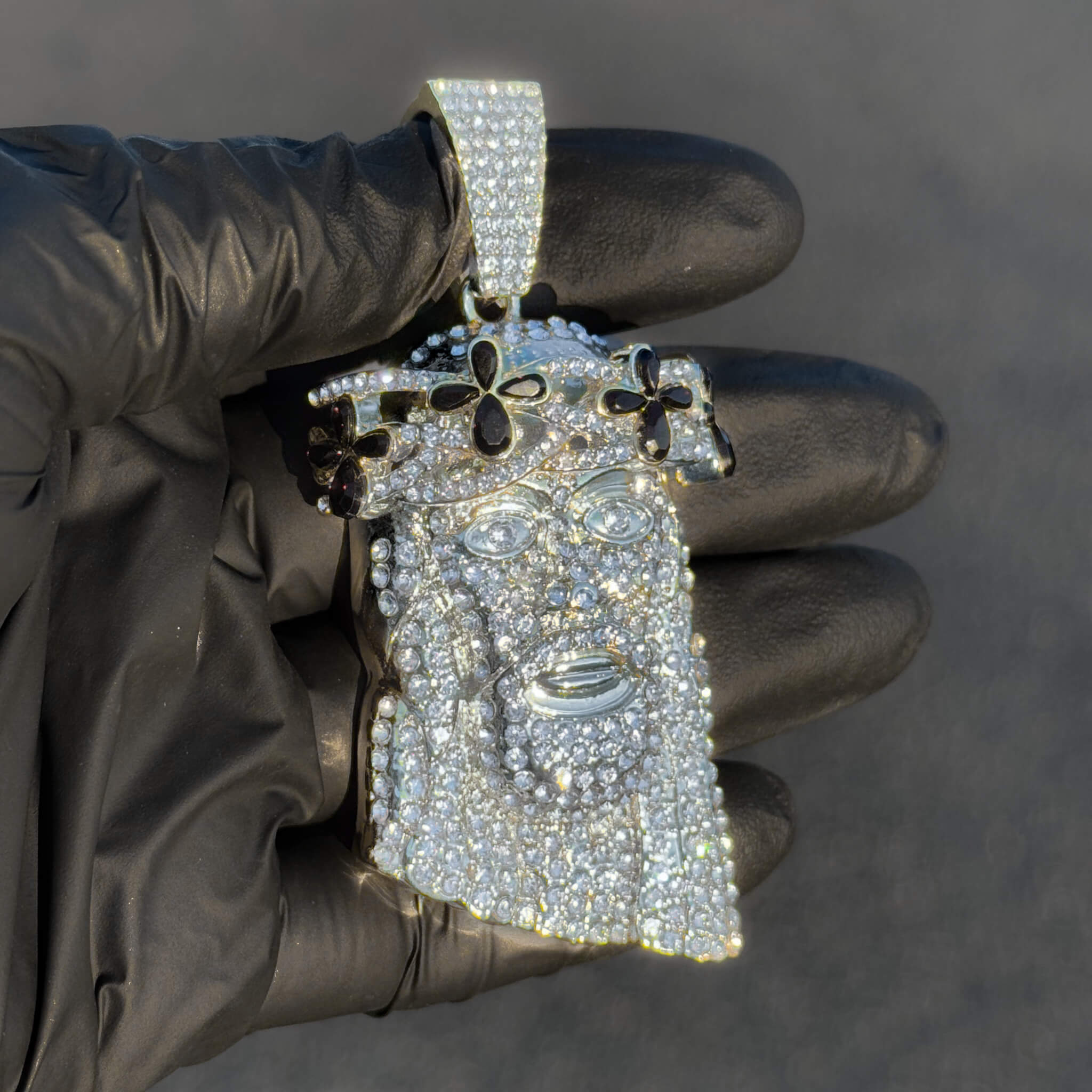 Silver iced-out Jesus pendant featuring black floral gemstones shown in glove for detail view.