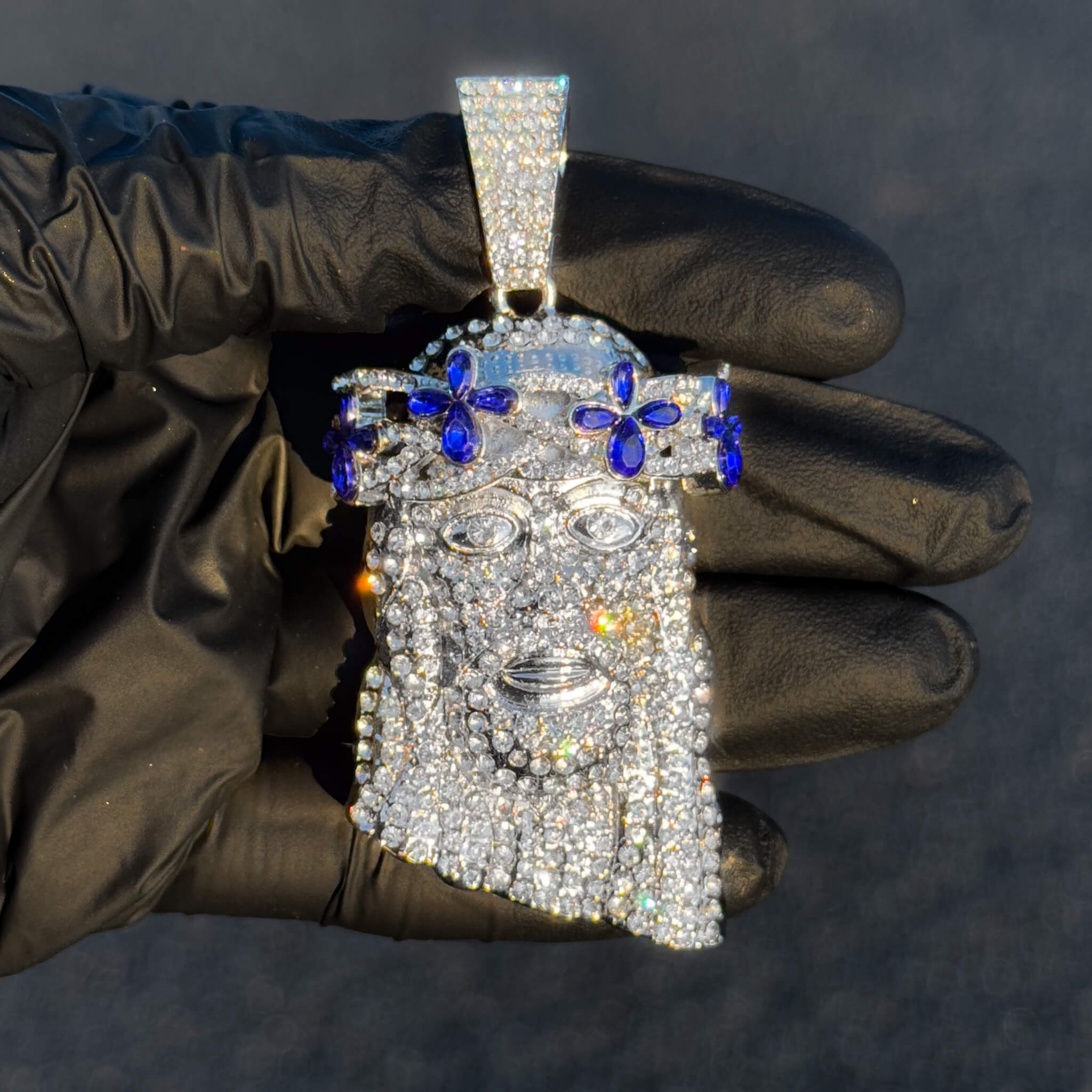 Silver iced-out Jesus pendant with blue floral gemstones held in glove for high-detail viewing.
