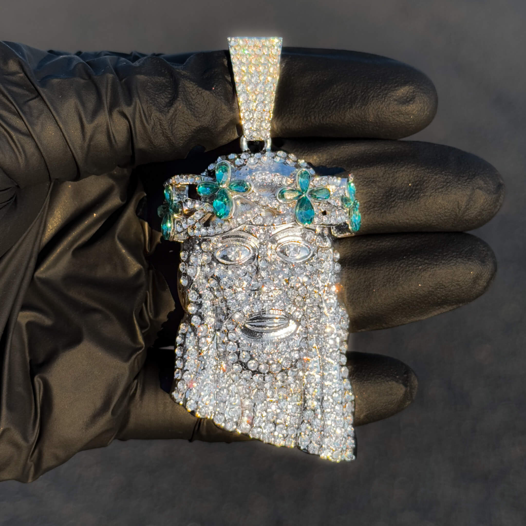 Silver iced-out Jesus pendant with teal floral gemstones shown close-up for sparkling detail.