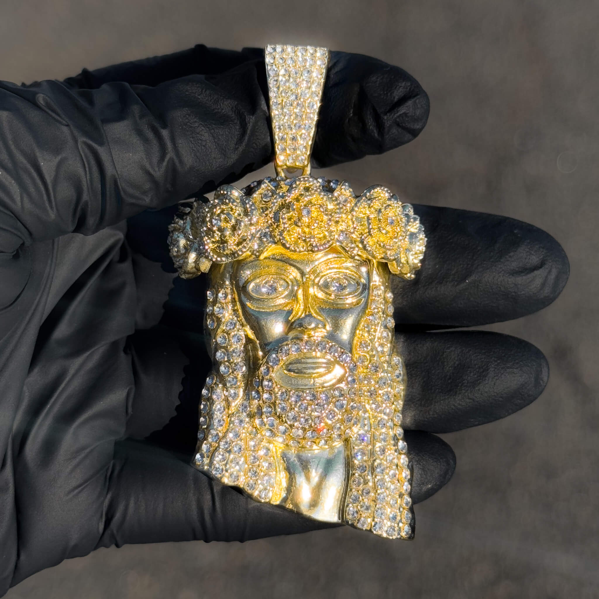 Gold iced-out Jesus crown pendant featuring rose accents and full stone detailing in sunlight.